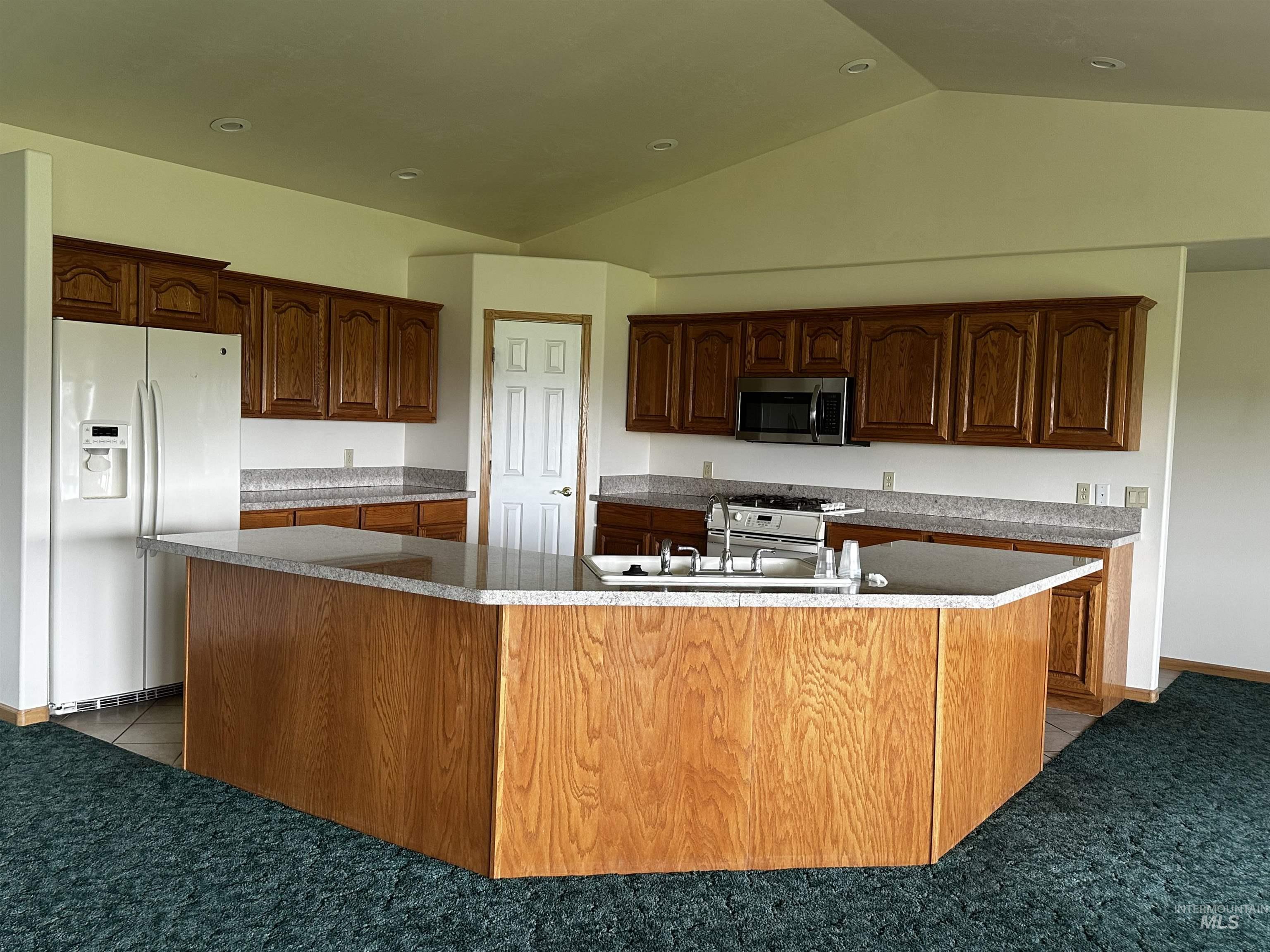 Kitchen with white appliances, a large island, vaulted ceiling, recessed lighting, and light colored carpet