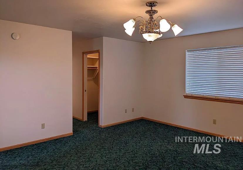 Unfurnished bedroom featuring dark carpet, a chandelier, and a walk in closet