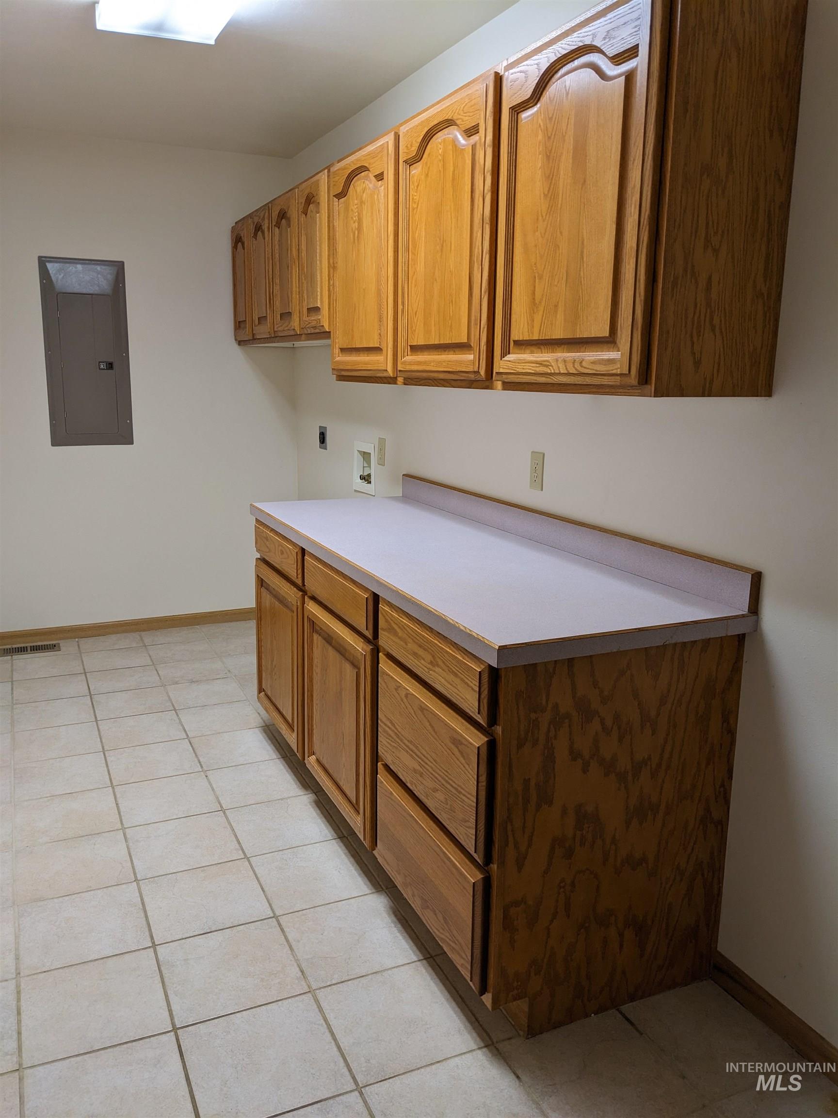 Kitchen featuring light countertops, light tile patterned floors, electric panel, and brown cabinetry