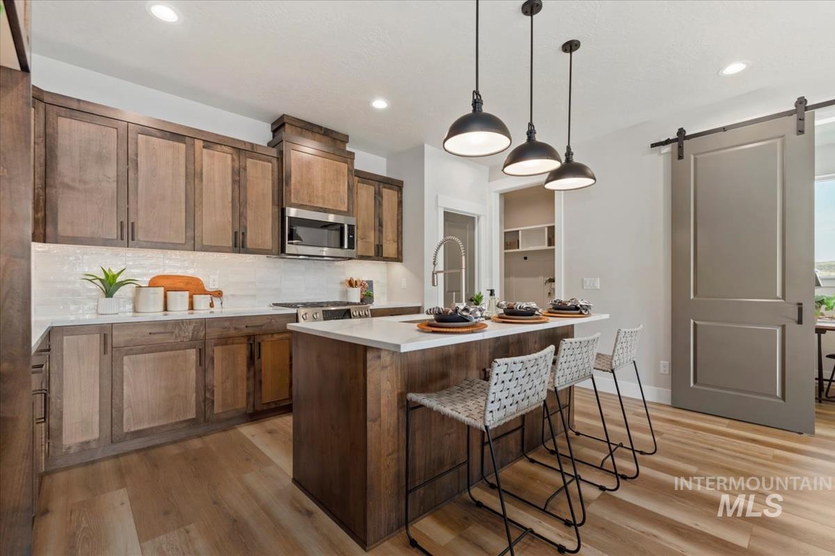 Kitchen with a barn door, a kitchen island with sink, a breakfast bar, decorative backsplash, and decorative light fixtures