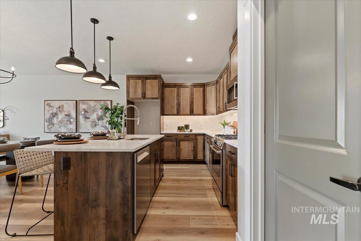 Kitchen featuring a breakfast bar area, stainless steel appliances, hanging light fixtures, light wood-type flooring, and tasteful backsplash