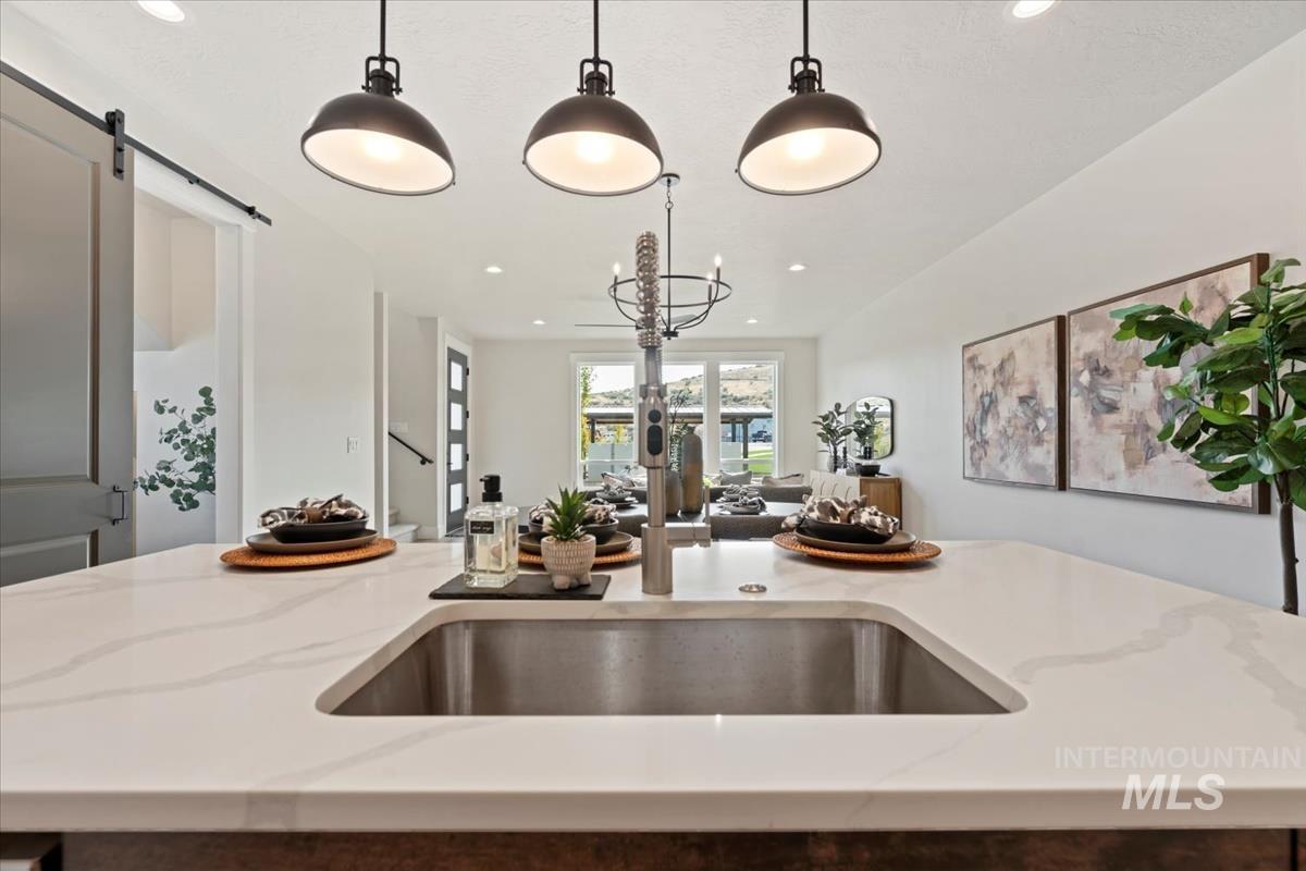 Kitchen with a barn door, light stone countertops, hanging light fixtures, a center island with sink, and recessed lighting