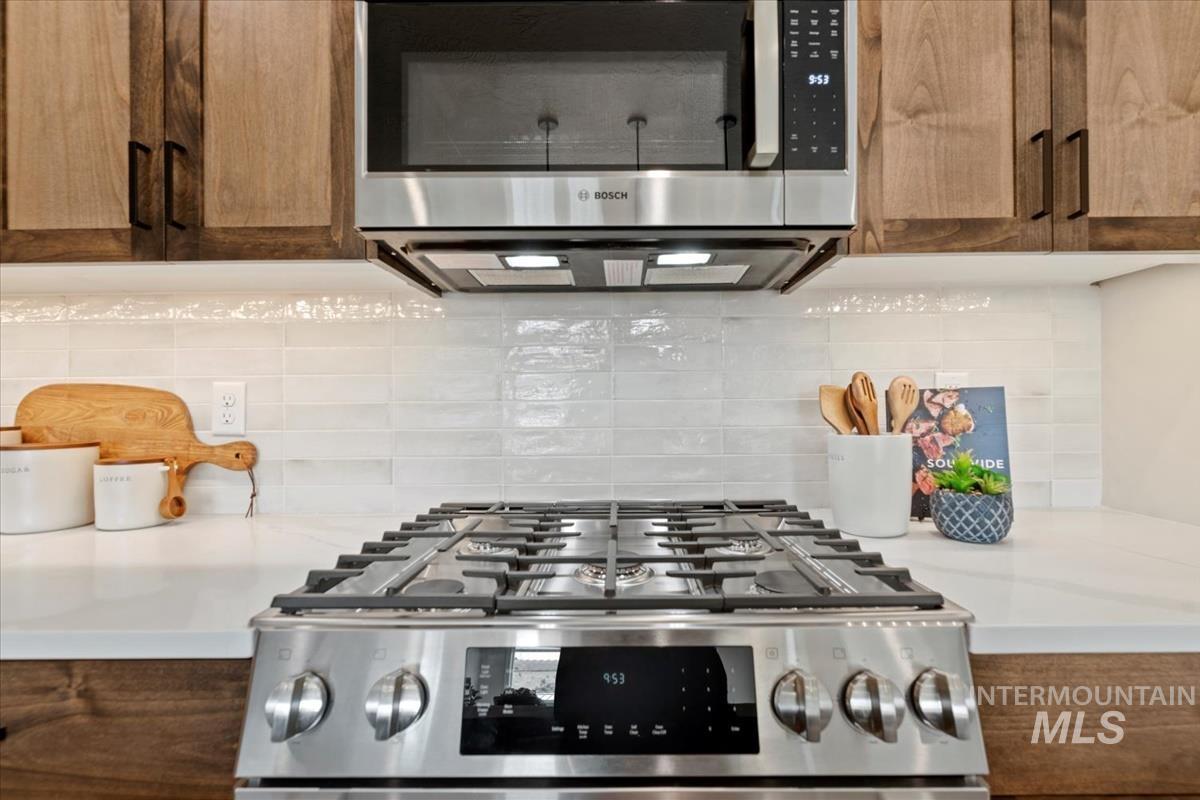 Kitchen view of stainless steel appliances, decorative backsplash, light stone countertops, and brown cabinets