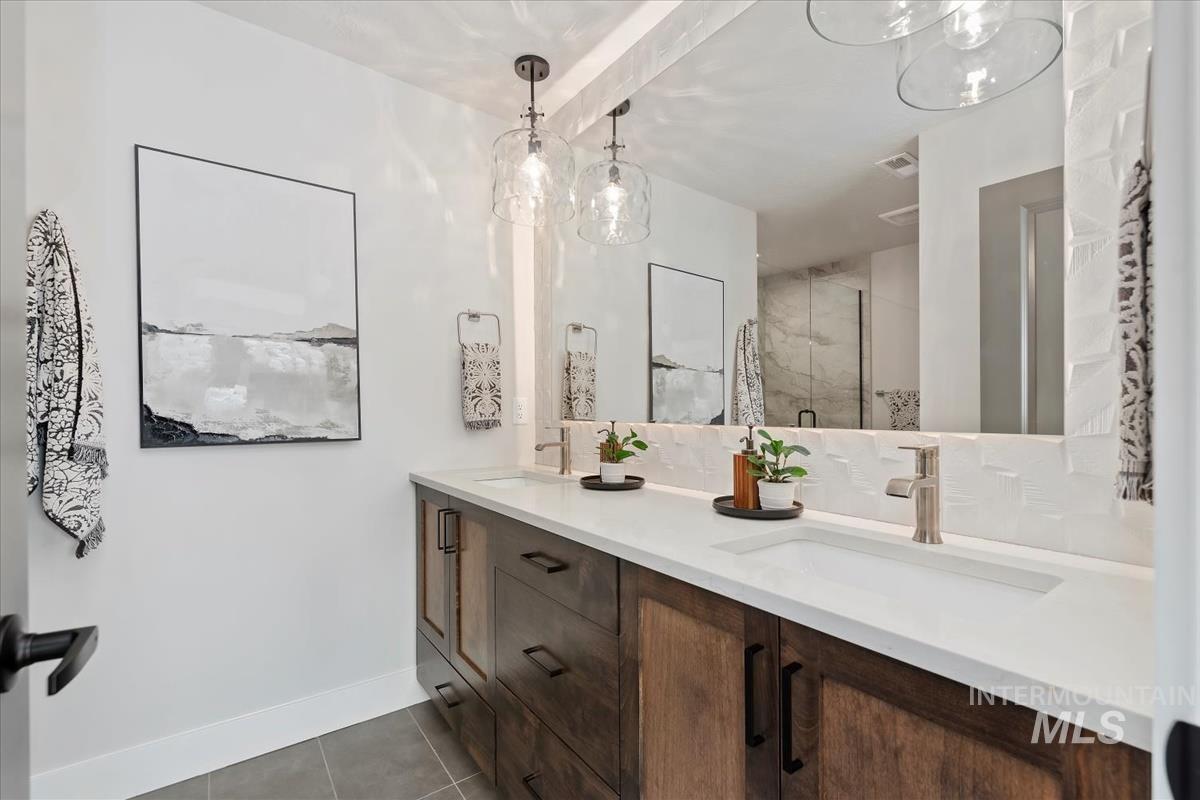 Bathroom with light tile patterned flooring, a marble finish shower, and double vanity