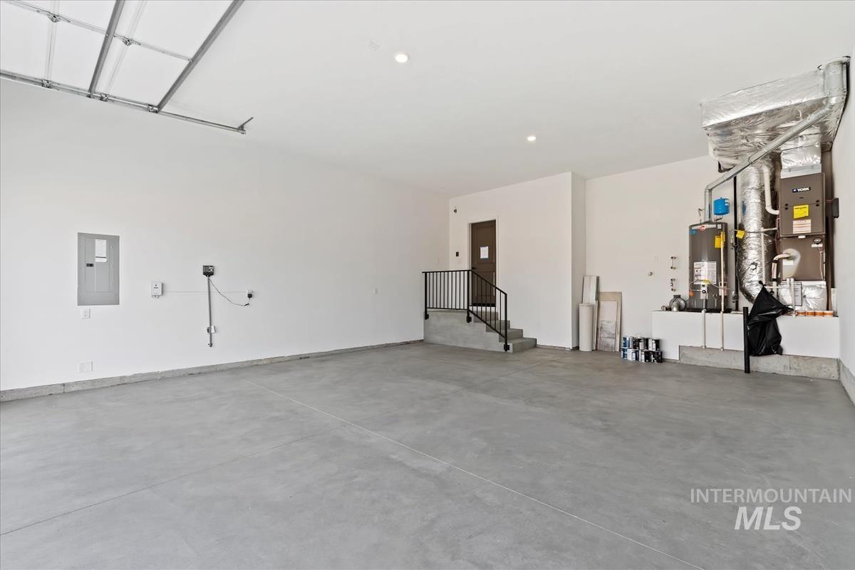 Garage featuring electric panel, water heater, and heating unit