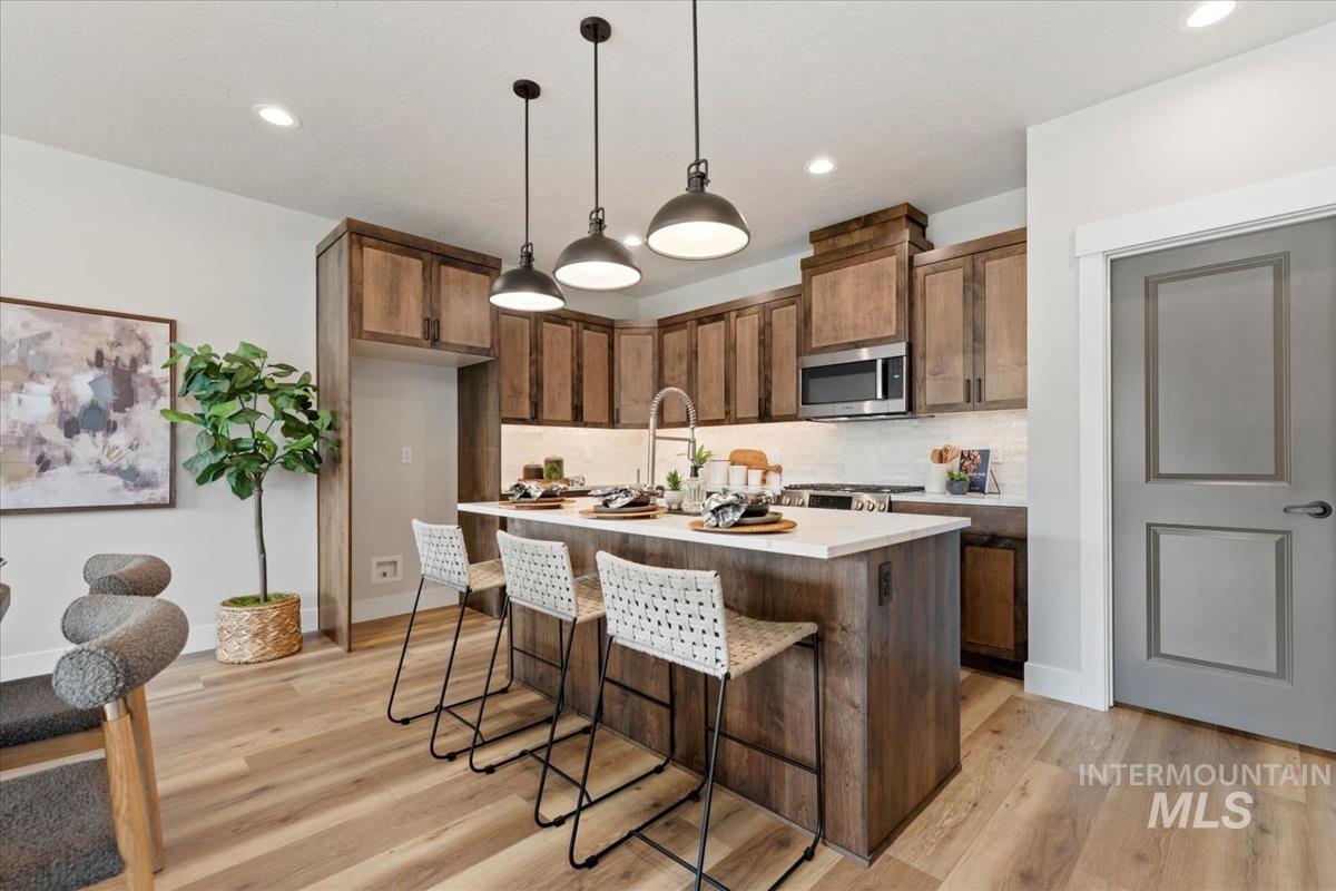 Kitchen with a breakfast bar area, pendant lighting, decorative backsplash, a kitchen island with sink, and light wood finished floors