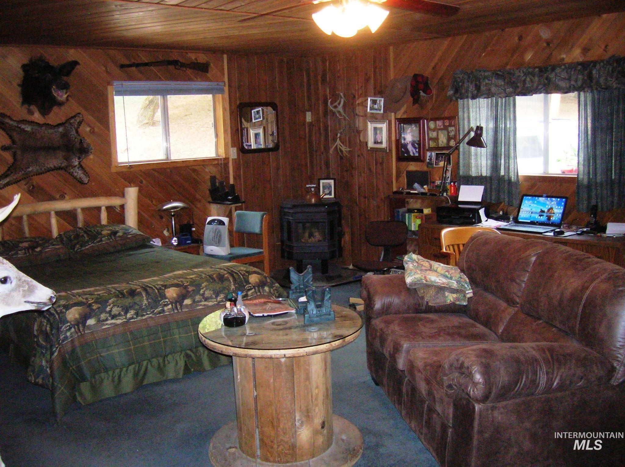 Carpeted living room featuring wooden ceiling, a wood stove, wood walls, healthy amount of natural light, and ceiling fan