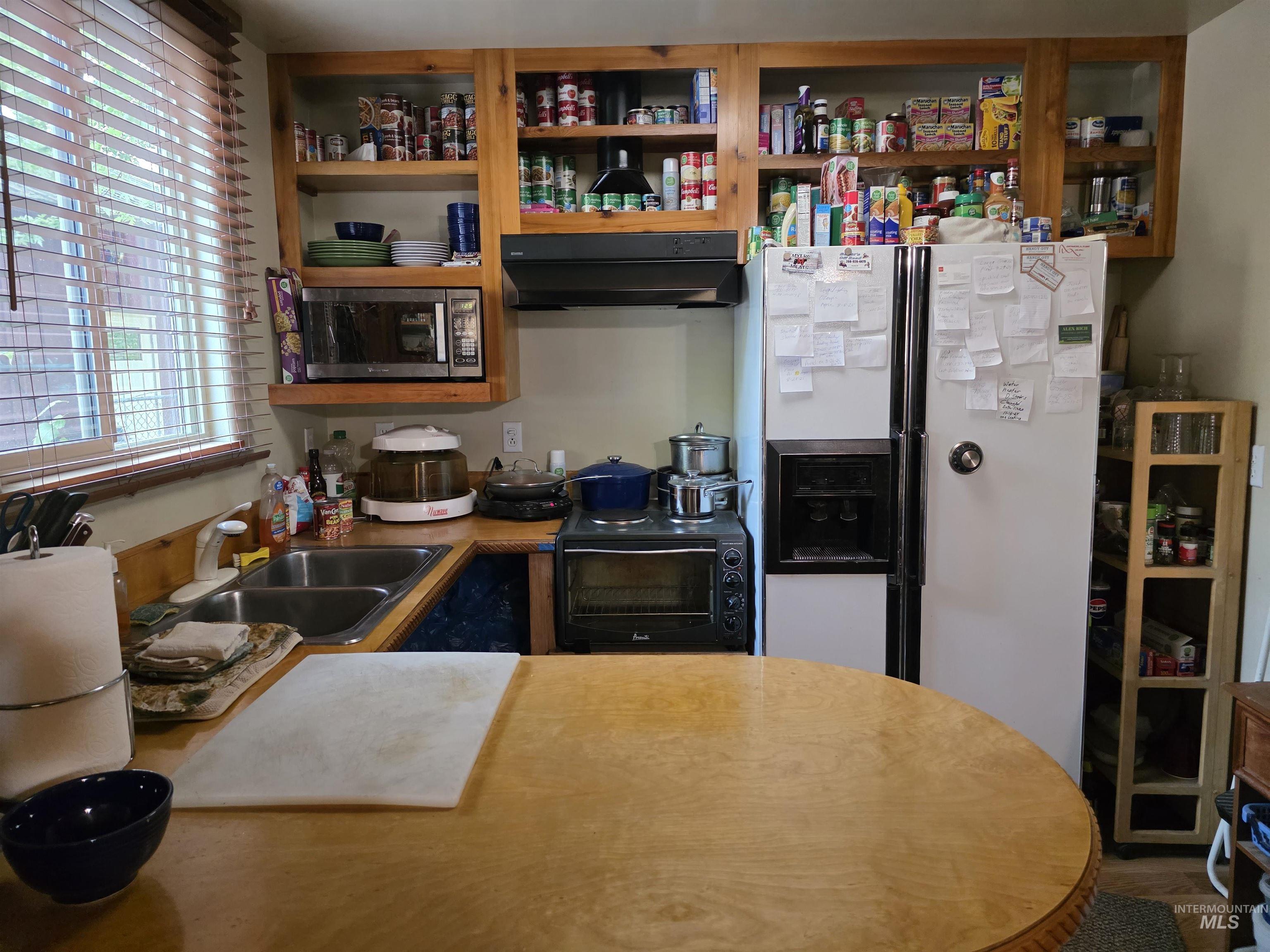 Kitchen featuring white fridge with ice dispenser, extractor fan, stainless steel microwave, black stove, and light countertops