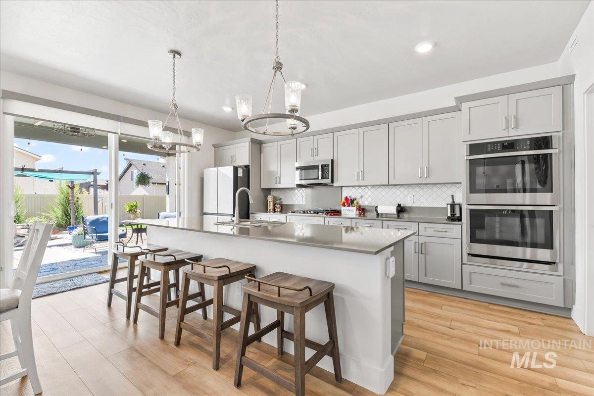 Kitchen featuring tasteful backsplash, a kitchen breakfast bar, appliances with stainless steel finishes, hanging light fixtures, and light wood-style flooring