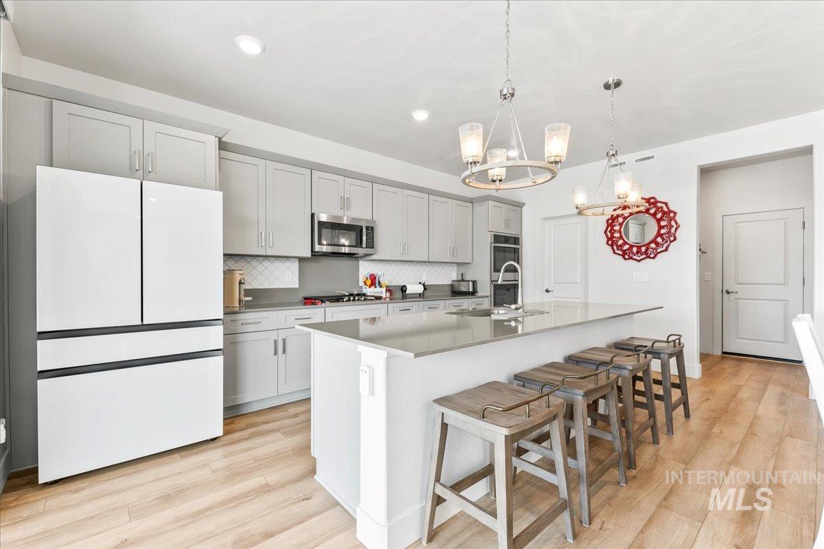 Kitchen featuring decorative backsplash, light wood-style flooring, a breakfast bar area, hanging light fixtures, and appliances with stainless steel finishes