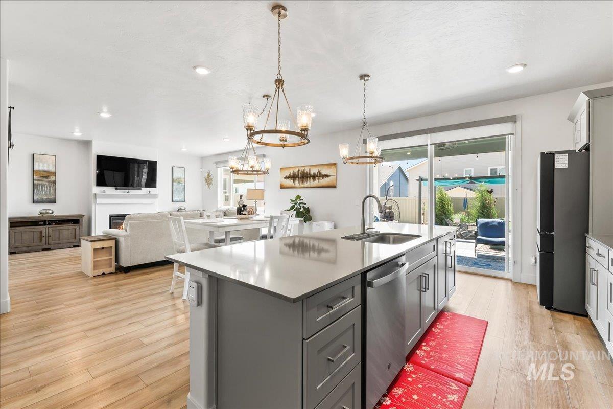 Kitchen featuring open floor plan, a kitchen island with sink, a chandelier, freestanding refrigerator, and a warm lit fireplace