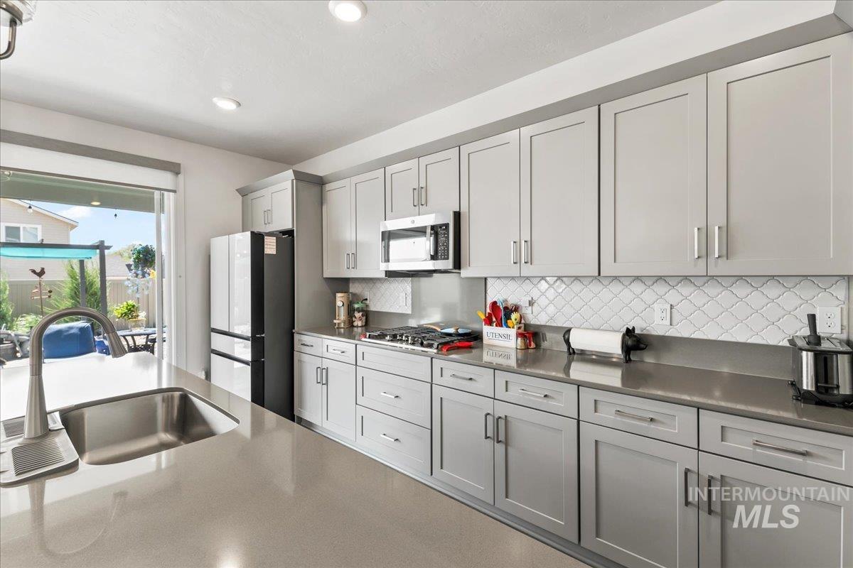 Kitchen featuring stainless steel appliances, tasteful backsplash, gray cabinets, light stone countertops, and recessed lighting