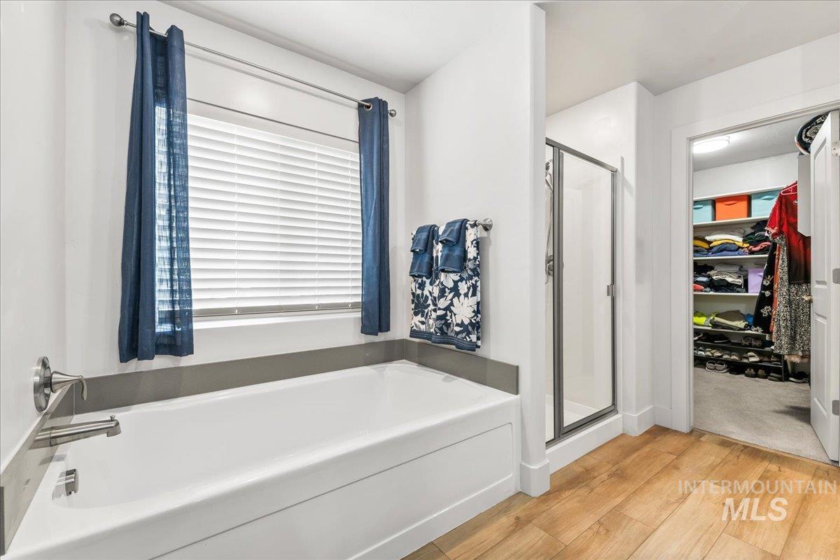 Bathroom with a spacious closet, a shower stall, light wood finished floors, and a garden tub
