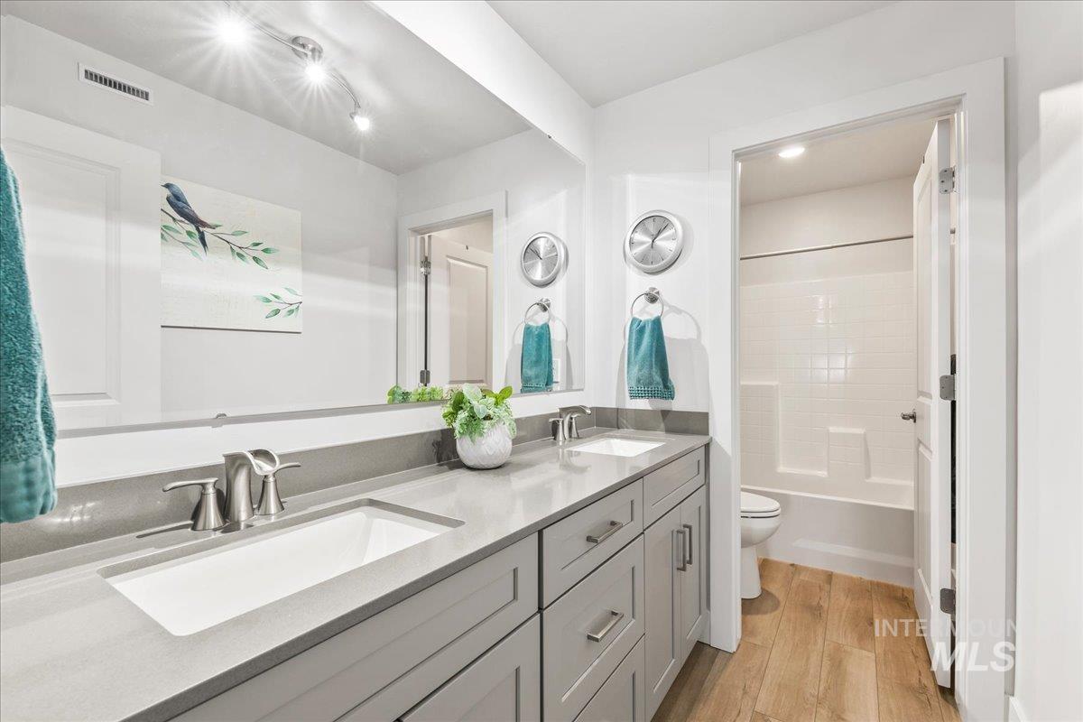 Bathroom with light wood-style floors, double vanity, and shower / bath combination