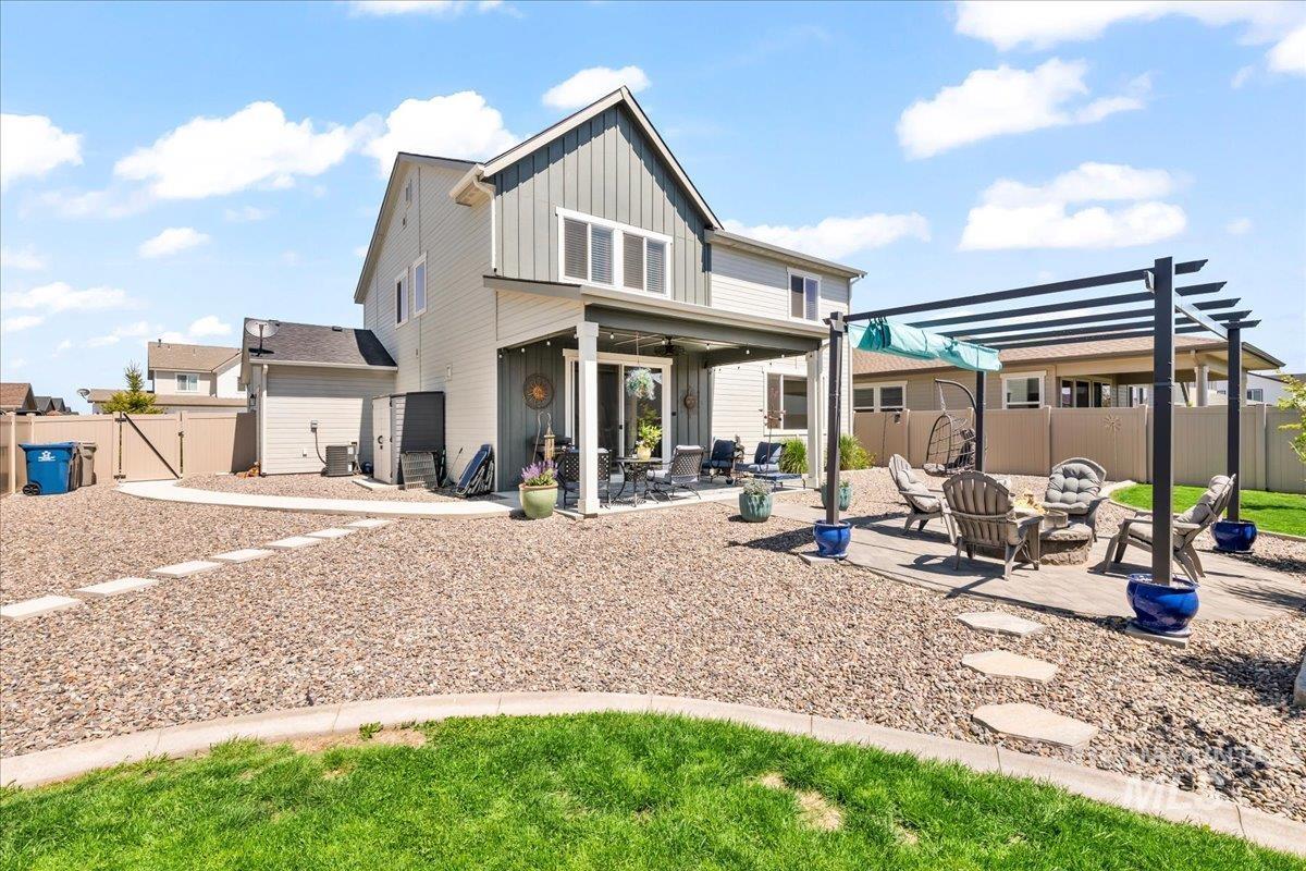 Back of property with board and batten siding, a patio area, a fenced backyard, an outdoor fire pit, and a gate