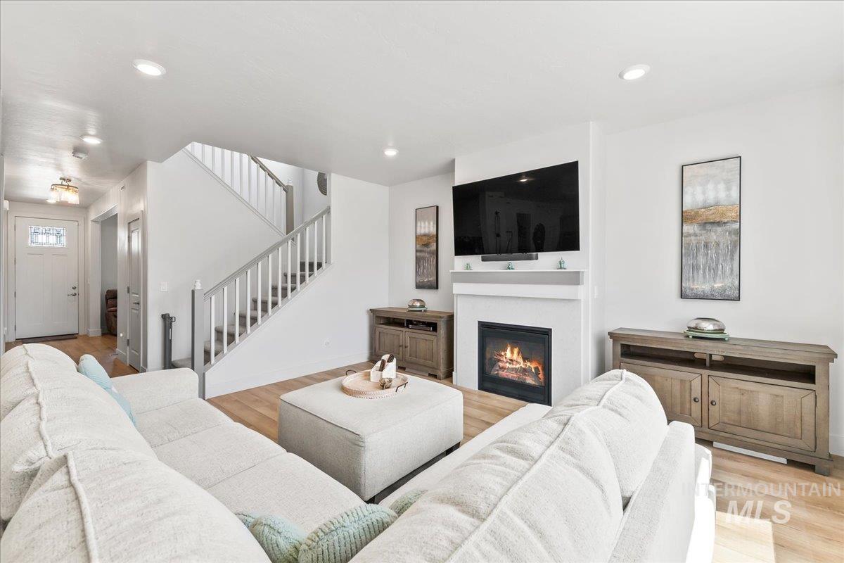 Living room with light wood-style flooring, stairway, a glass covered fireplace, and recessed lighting