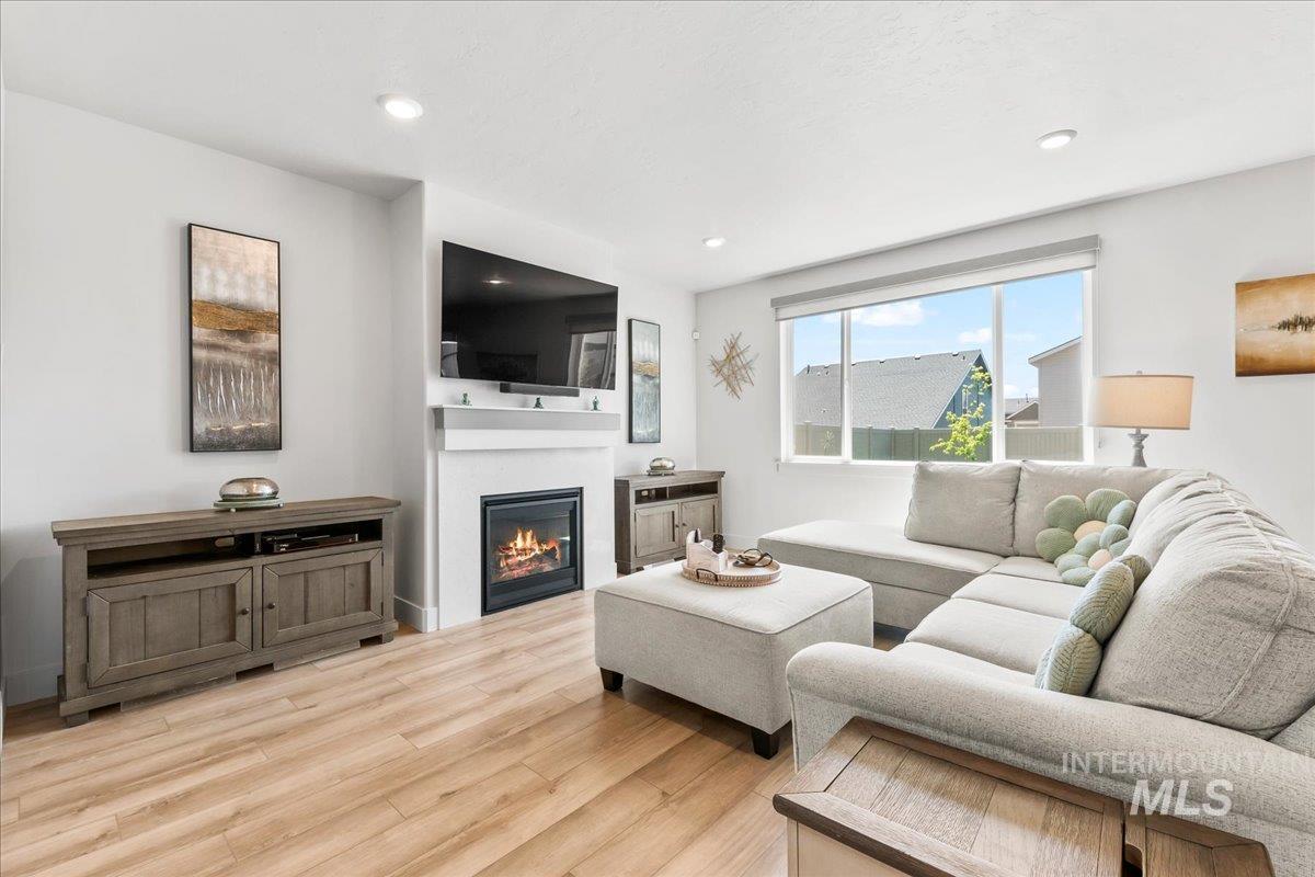 Living room featuring light wood-style floors, a glass covered fireplace, and recessed lighting