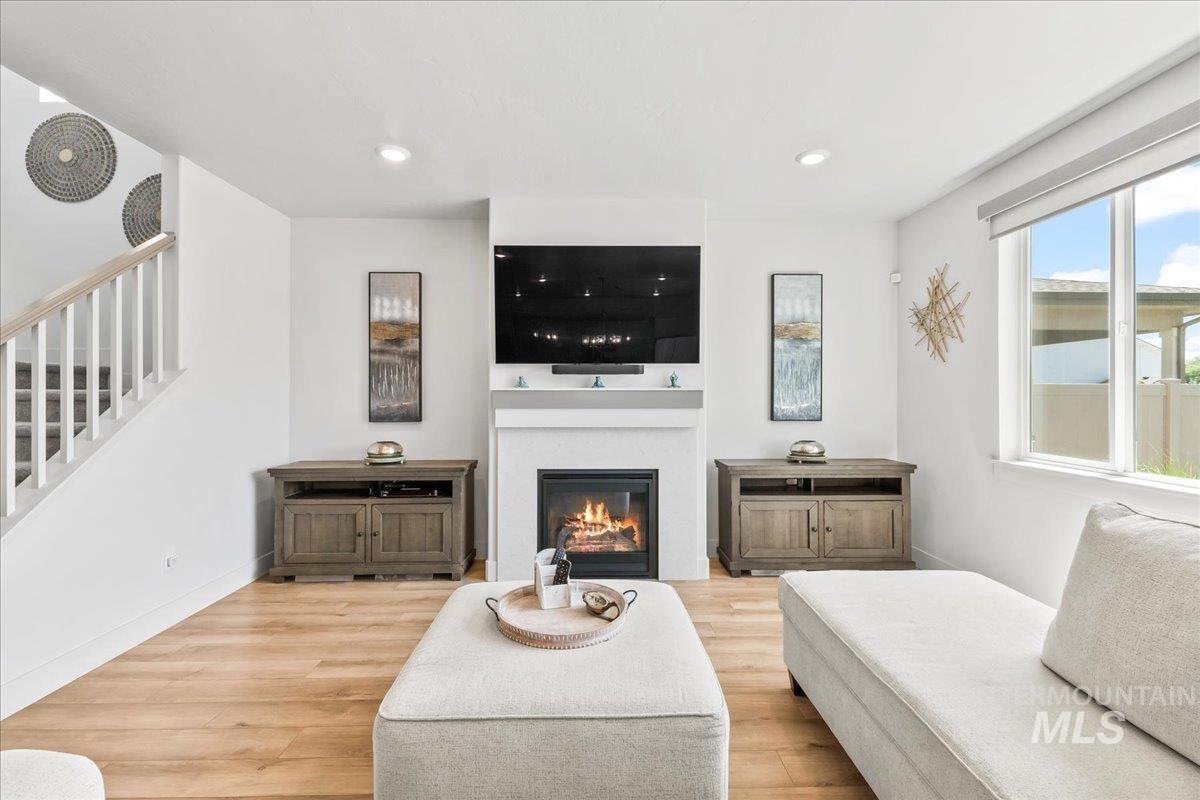 Living area featuring light wood-type flooring, stairs, a glass covered fireplace, and recessed lighting