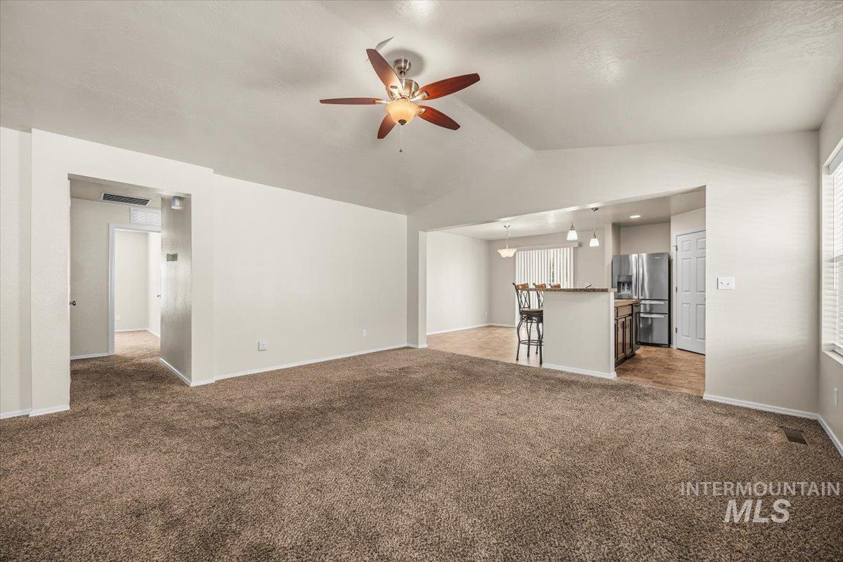 Unfurnished living room featuring dark carpet, lofted ceiling, and ceiling fan