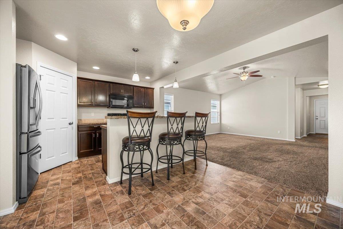 Kitchen featuring a kitchen breakfast bar, dark brown cabinetry, stainless steel refrigerator with ice dispenser, decorative light fixtures, and open floor plan