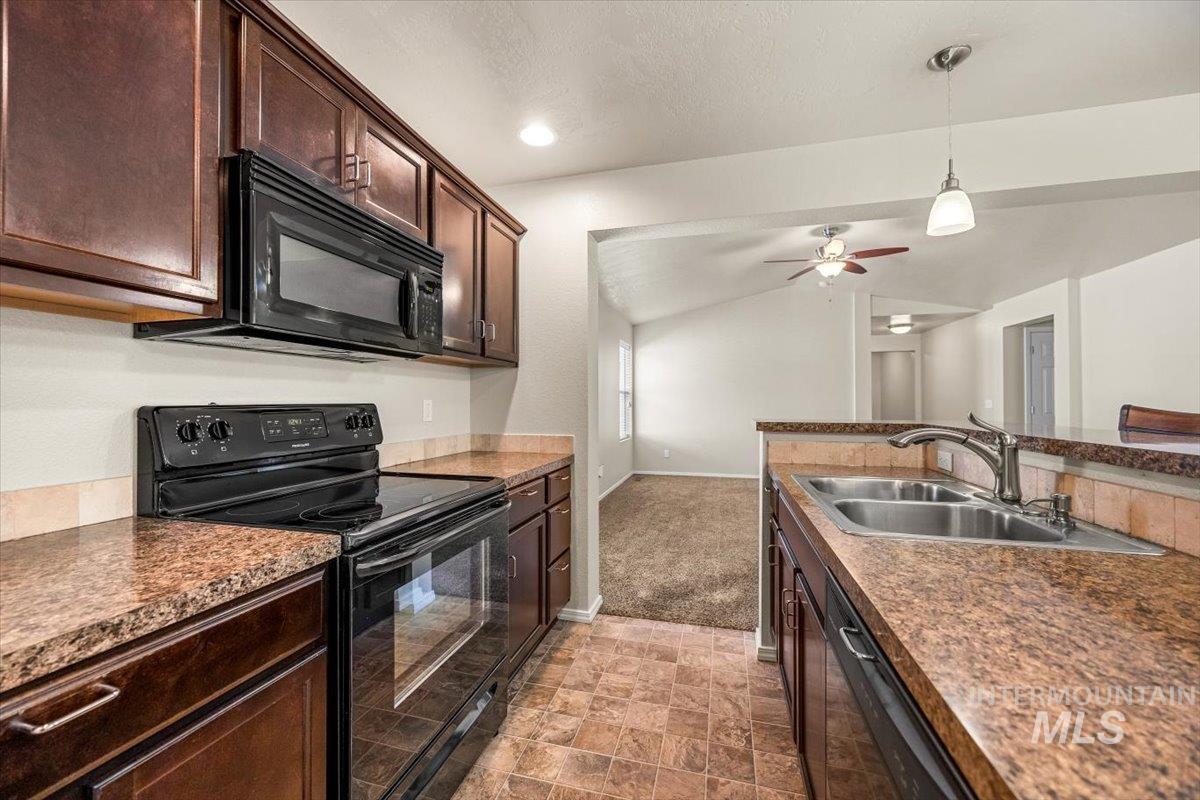 Kitchen featuring black appliances, hanging light fixtures, dark brown cabinets, lofted ceiling, and stone finish flooring