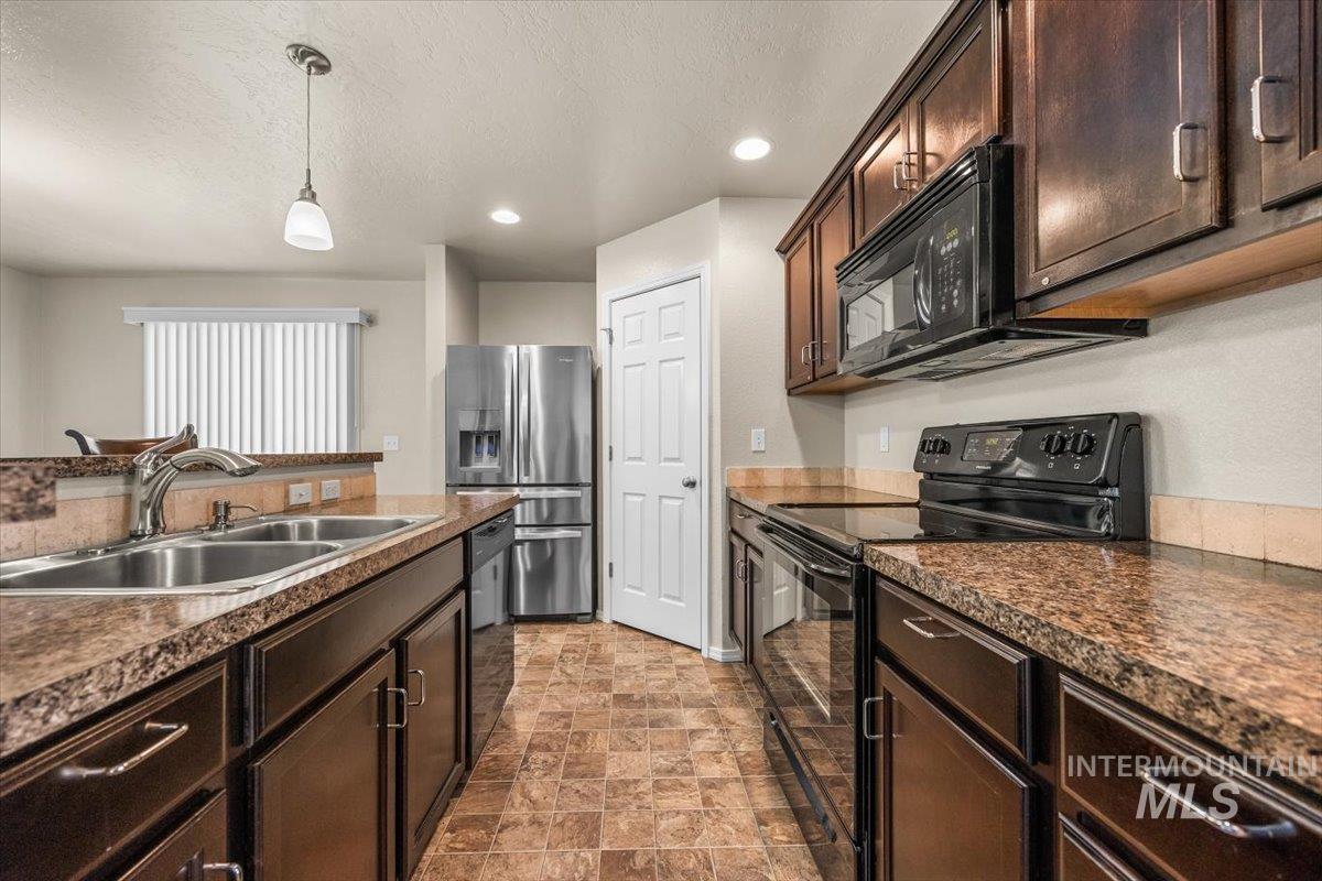 Kitchen with black appliances, dark brown cabinets, dark countertops, recessed lighting, and pendant lighting
