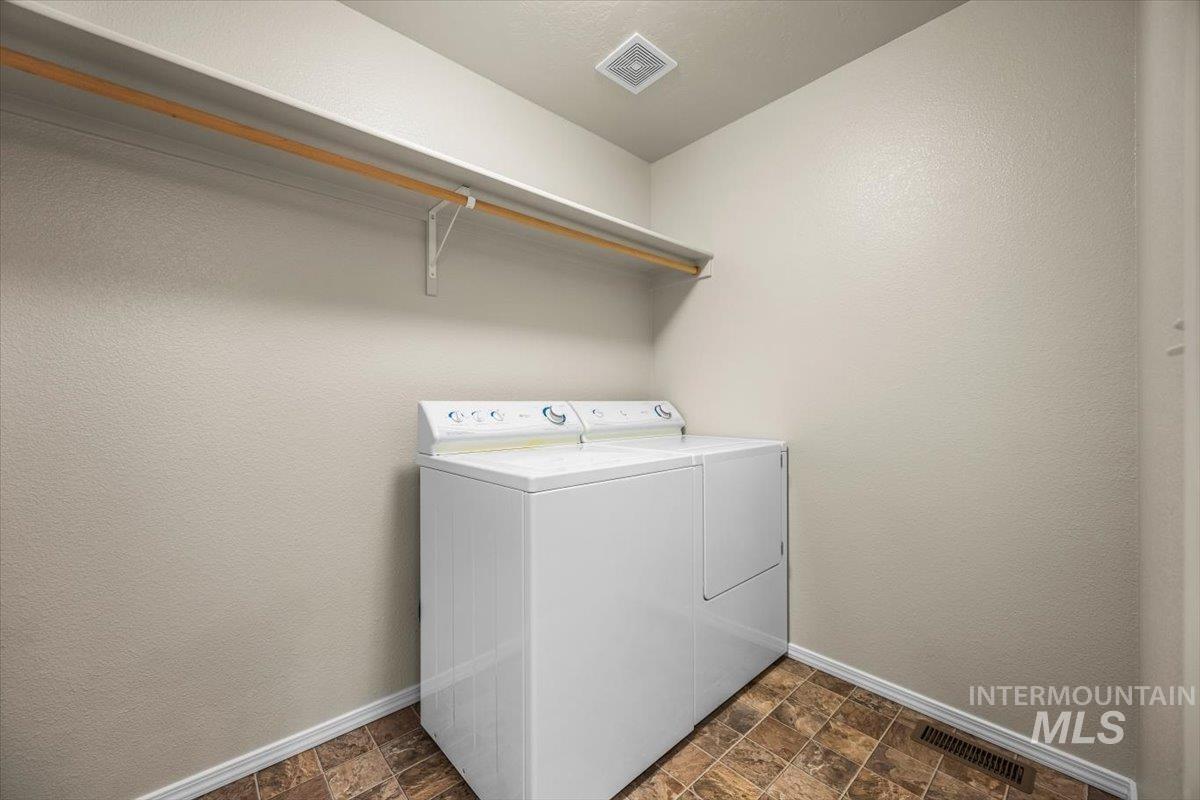 Laundry room with stone finish flooring, a textured wall, and washing machine and dryer