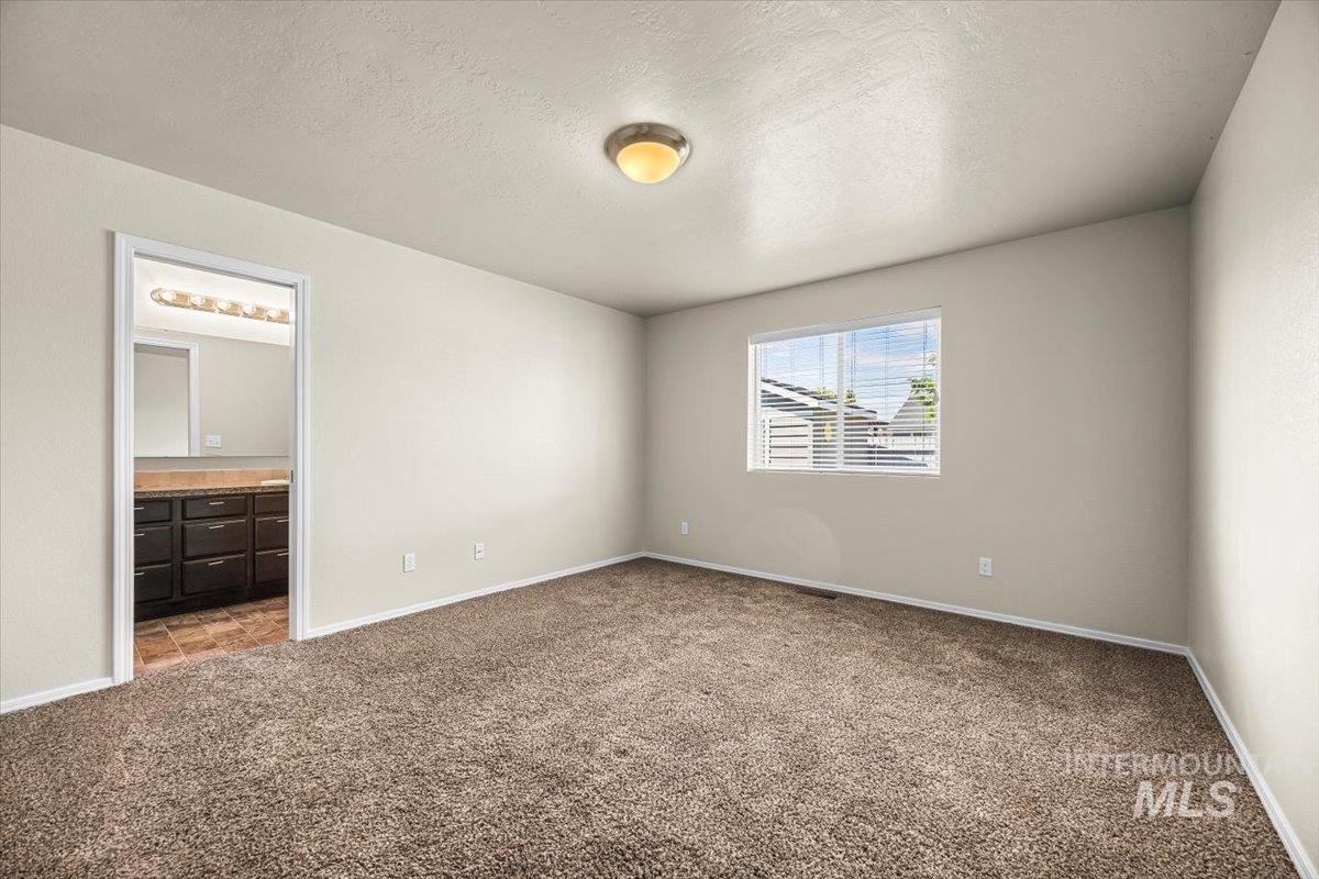 Unfurnished bedroom with a textured ceiling, carpet flooring, and ensuite bath