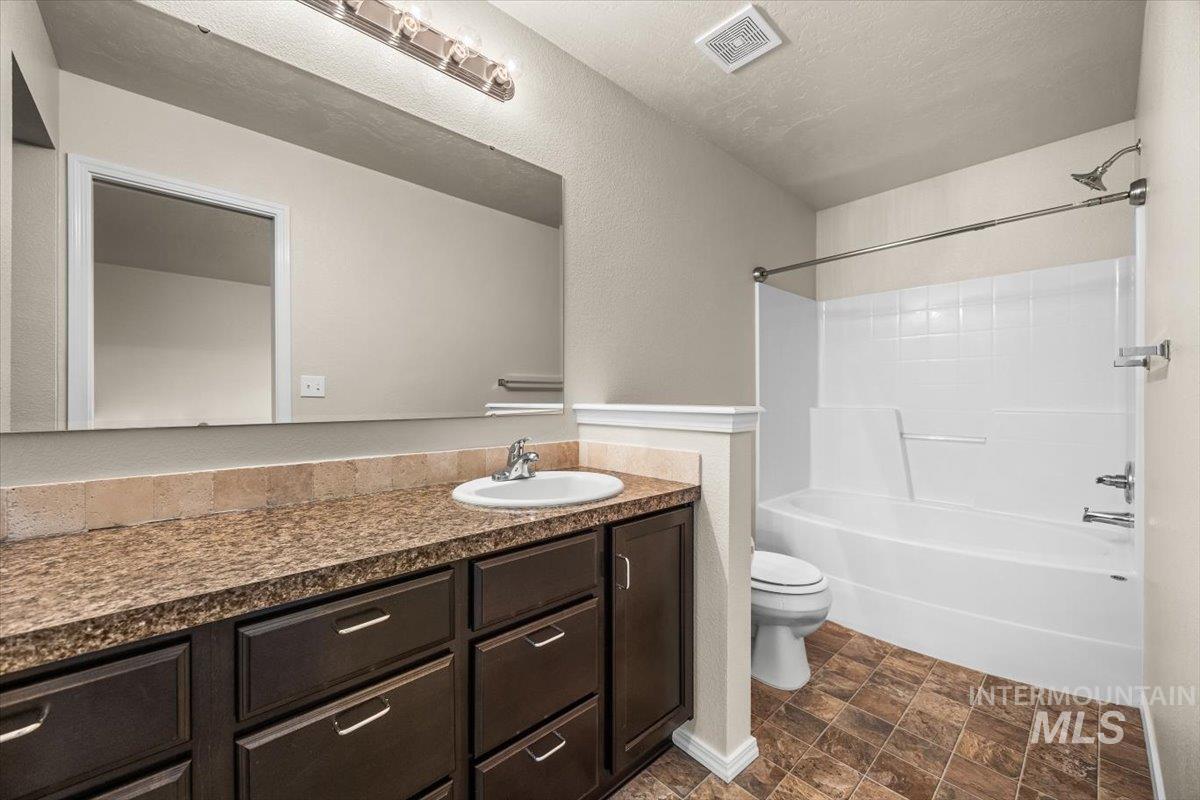 Full bath with bathing tub / shower combination, vanity, a textured wall, stone finish floors, and a textured ceiling