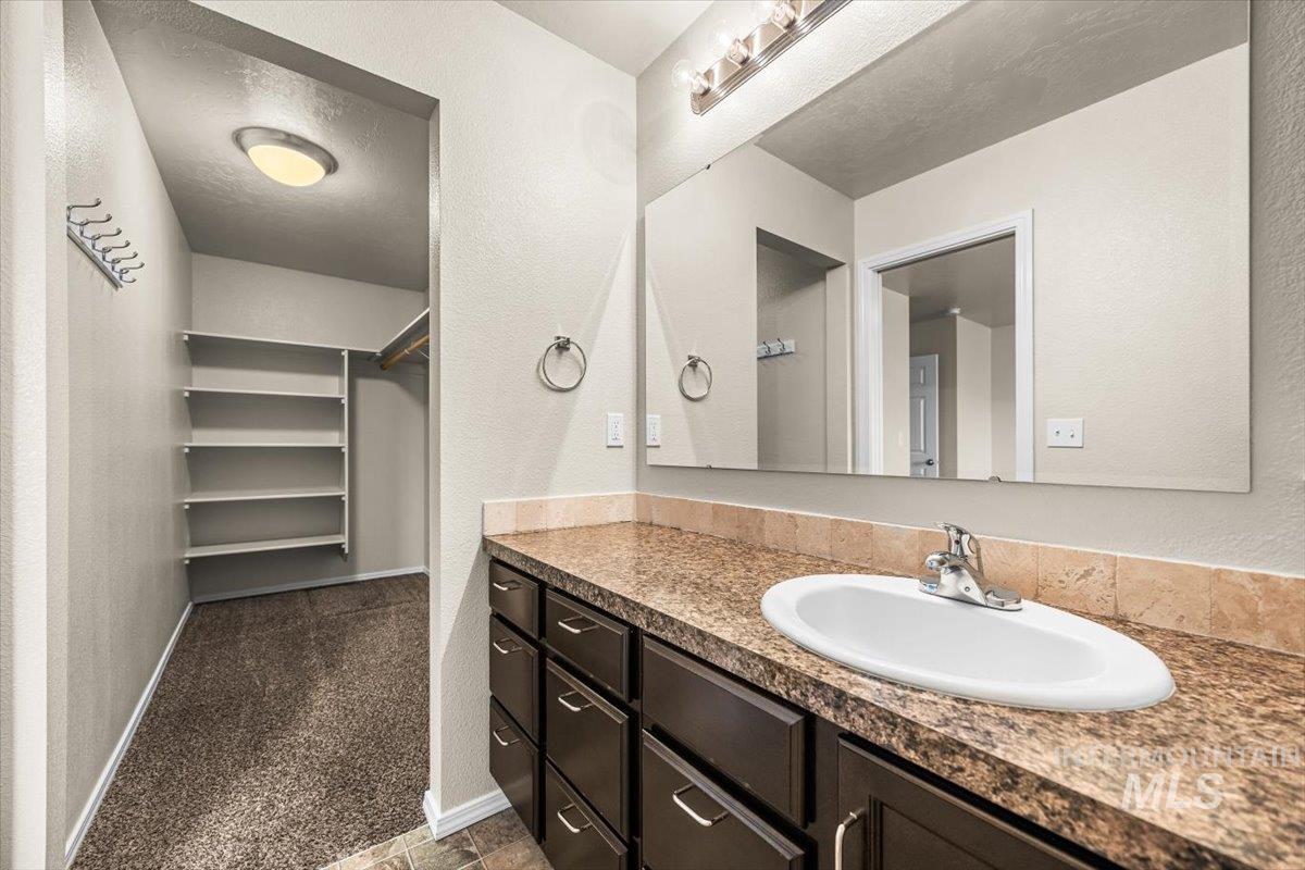 Bathroom featuring vanity, a textured wall, a spacious closet, and a textured ceiling