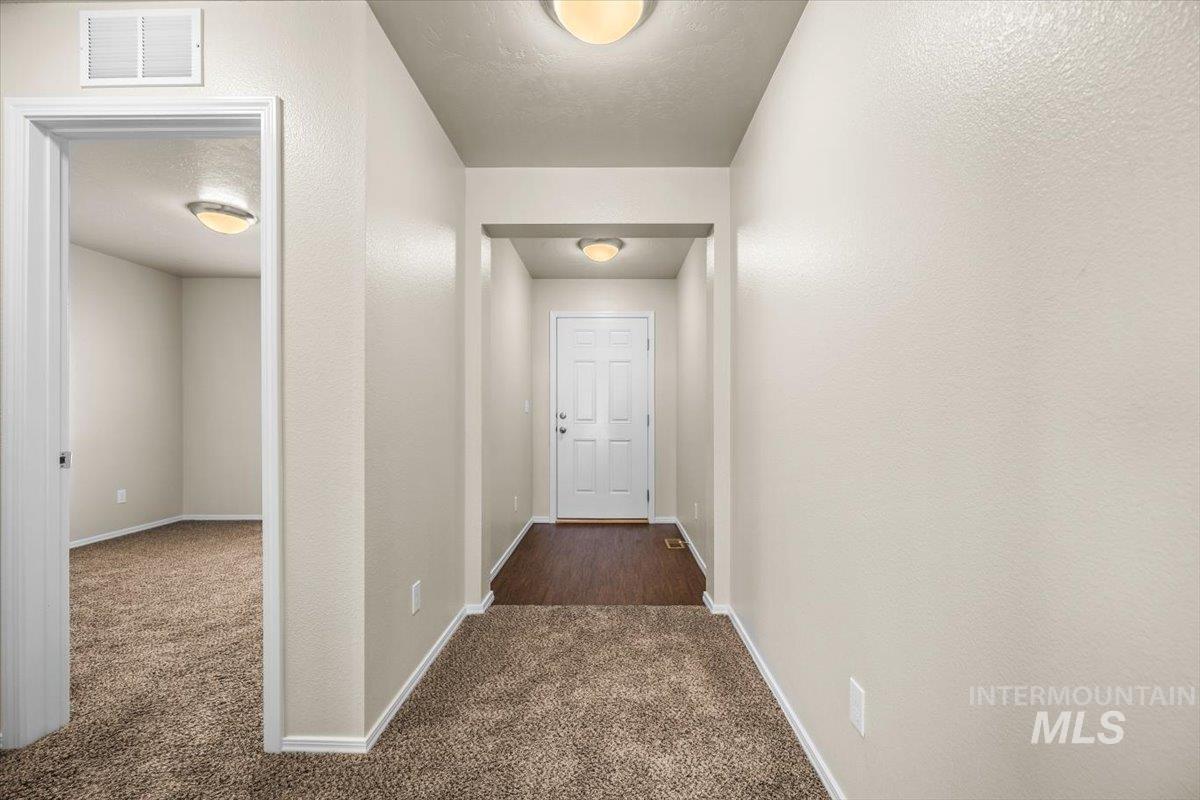 Hall featuring dark colored carpet, a textured ceiling, and a textured wall