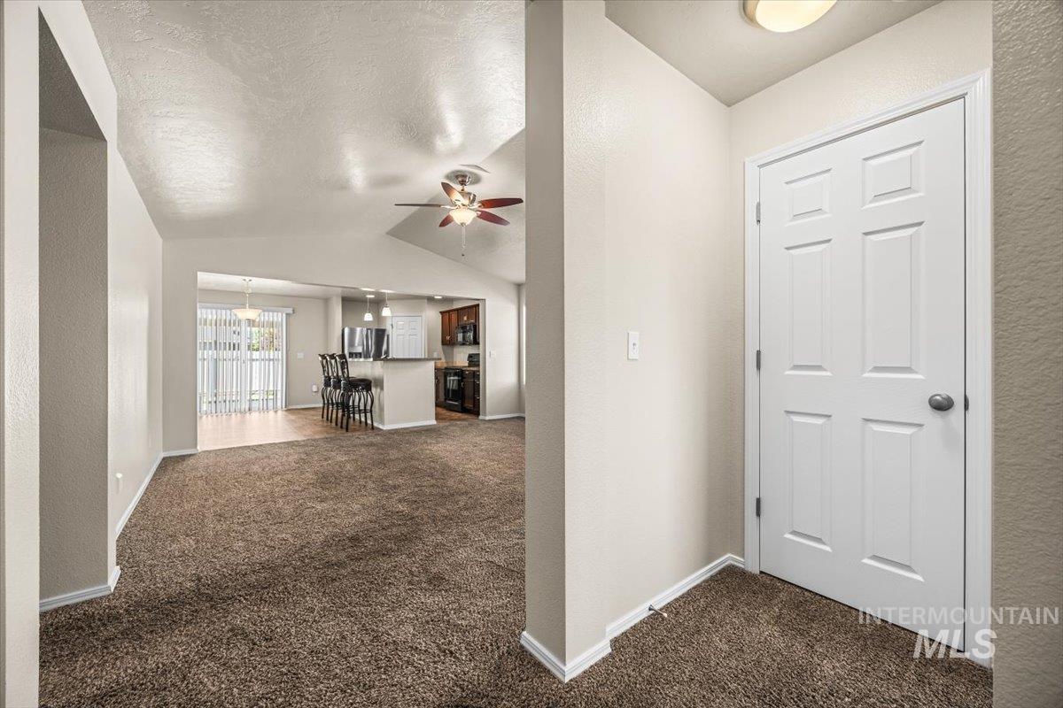 Entryway featuring lofted ceiling, dark carpet, a textured ceiling, ceiling fan, and a textured wall