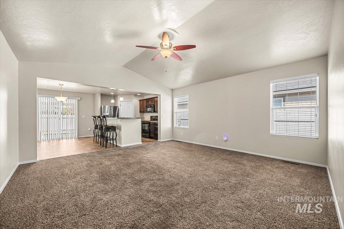 Unfurnished living room with vaulted ceiling, dark colored carpet, a ceiling fan, and a textured ceiling
