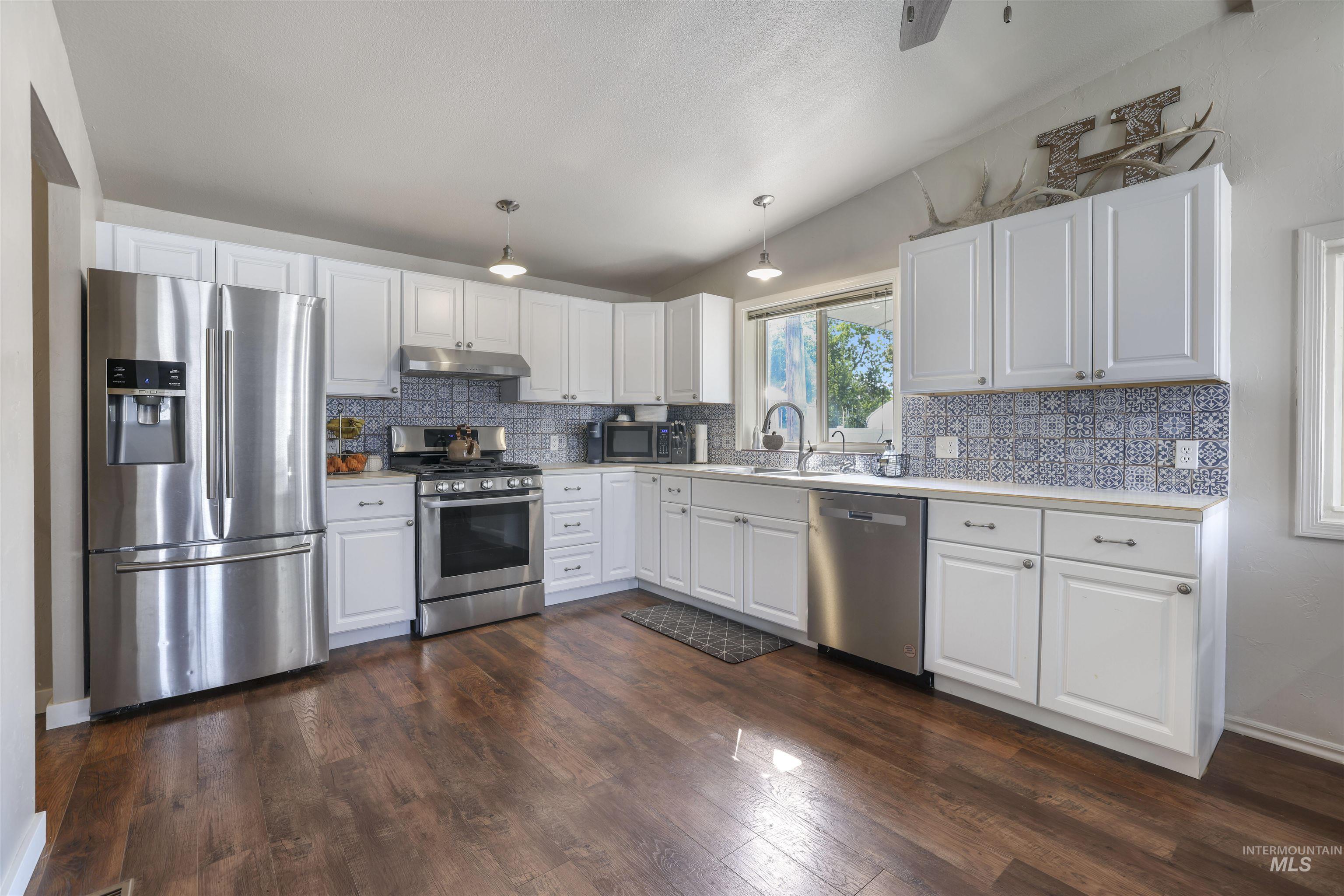Kitchen featuring white cabinetry, stainless steel appliances, light countertops, hanging light fixtures, and dark wood-style floors