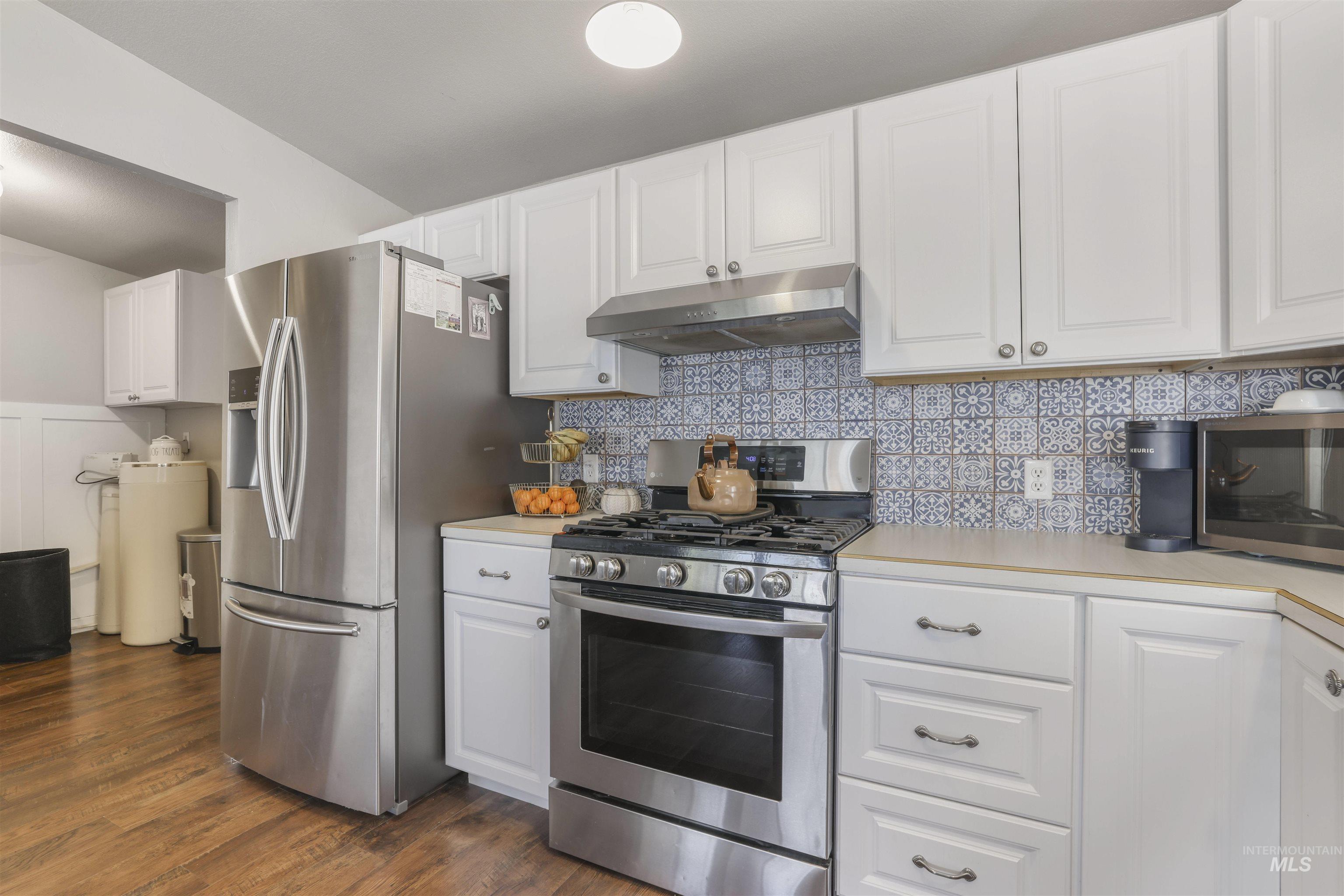 Kitchen featuring stainless steel appliances, white cabinets, light countertops, and under cabinet range hood