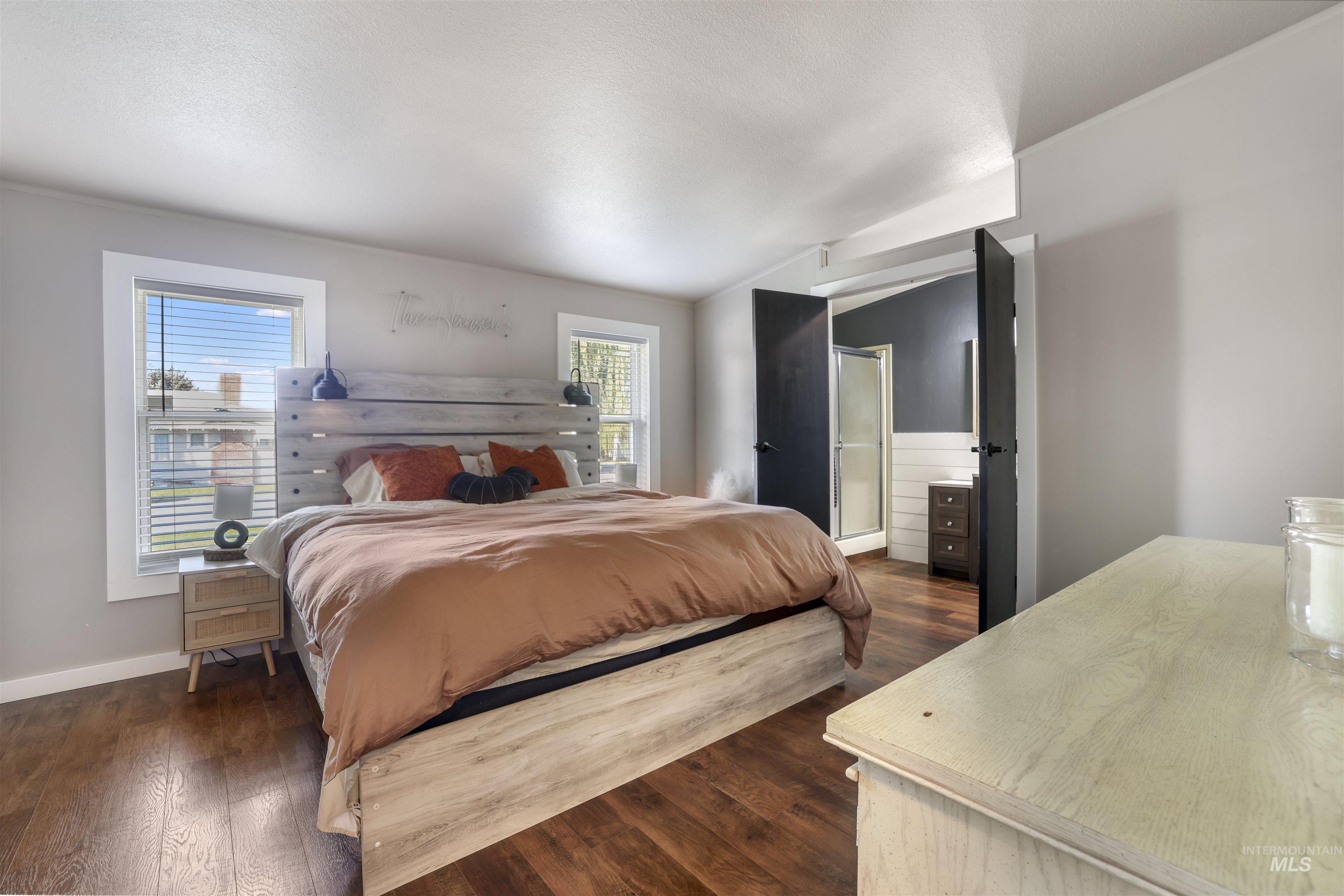 Bedroom featuring dark wood-style flooring, lofted ceiling, and ensuite bathroom