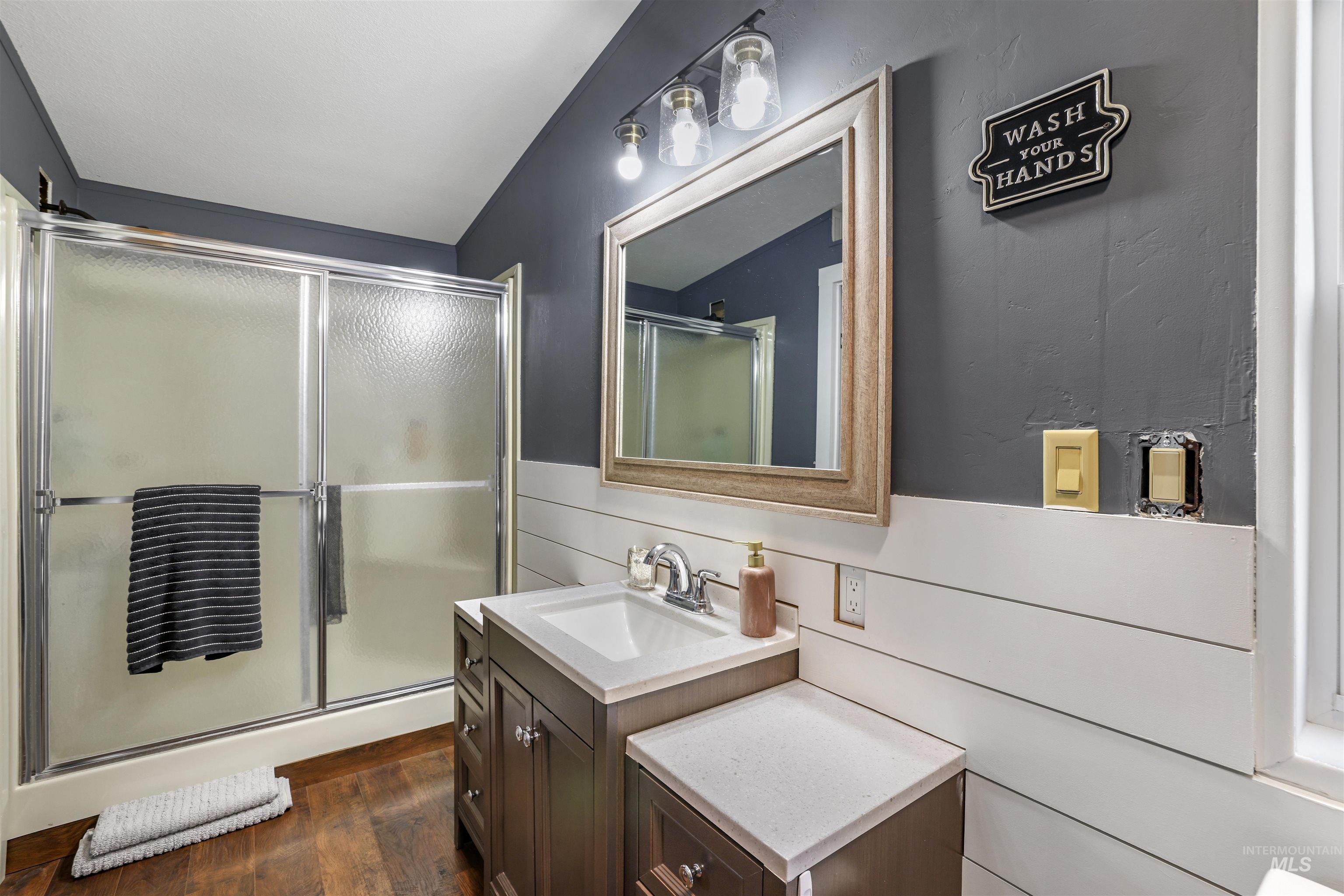 Bathroom with vanity, a shower stall, a wainscoted wall, and dark wood finished floors