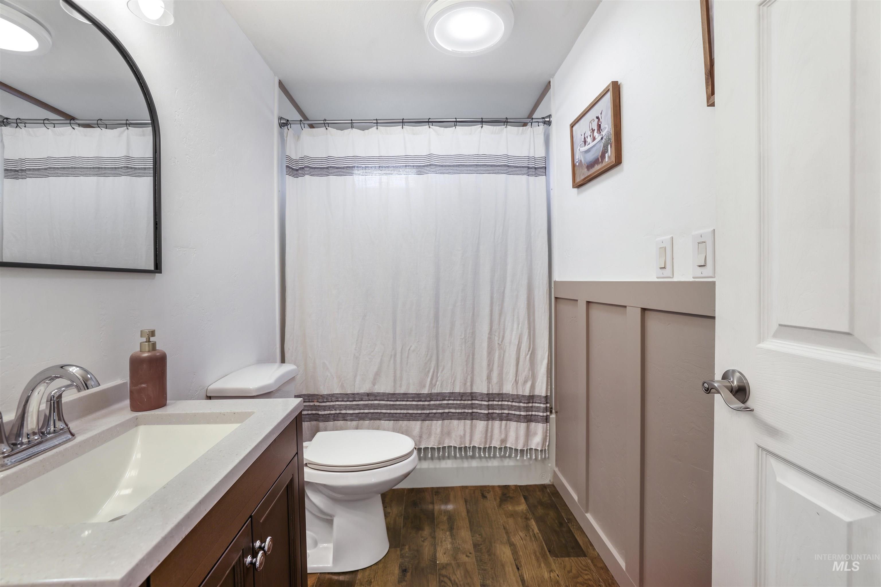 Bathroom with dark wood-style floors, vanity, and shower / bath combination with curtain