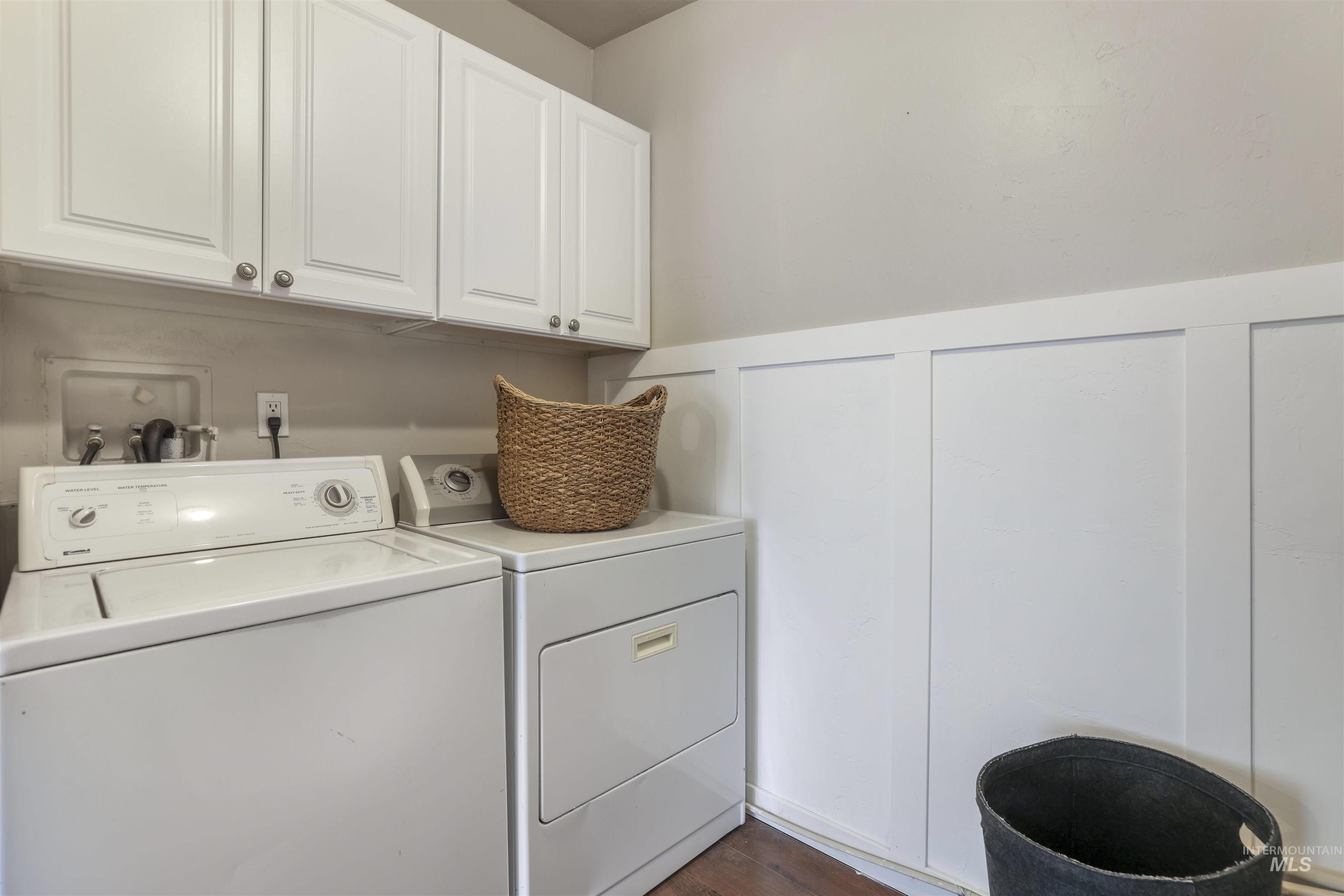 Laundry room featuring wainscoting, independent washer and dryer, cabinet space, dark wood-style floors, and a decorative wall