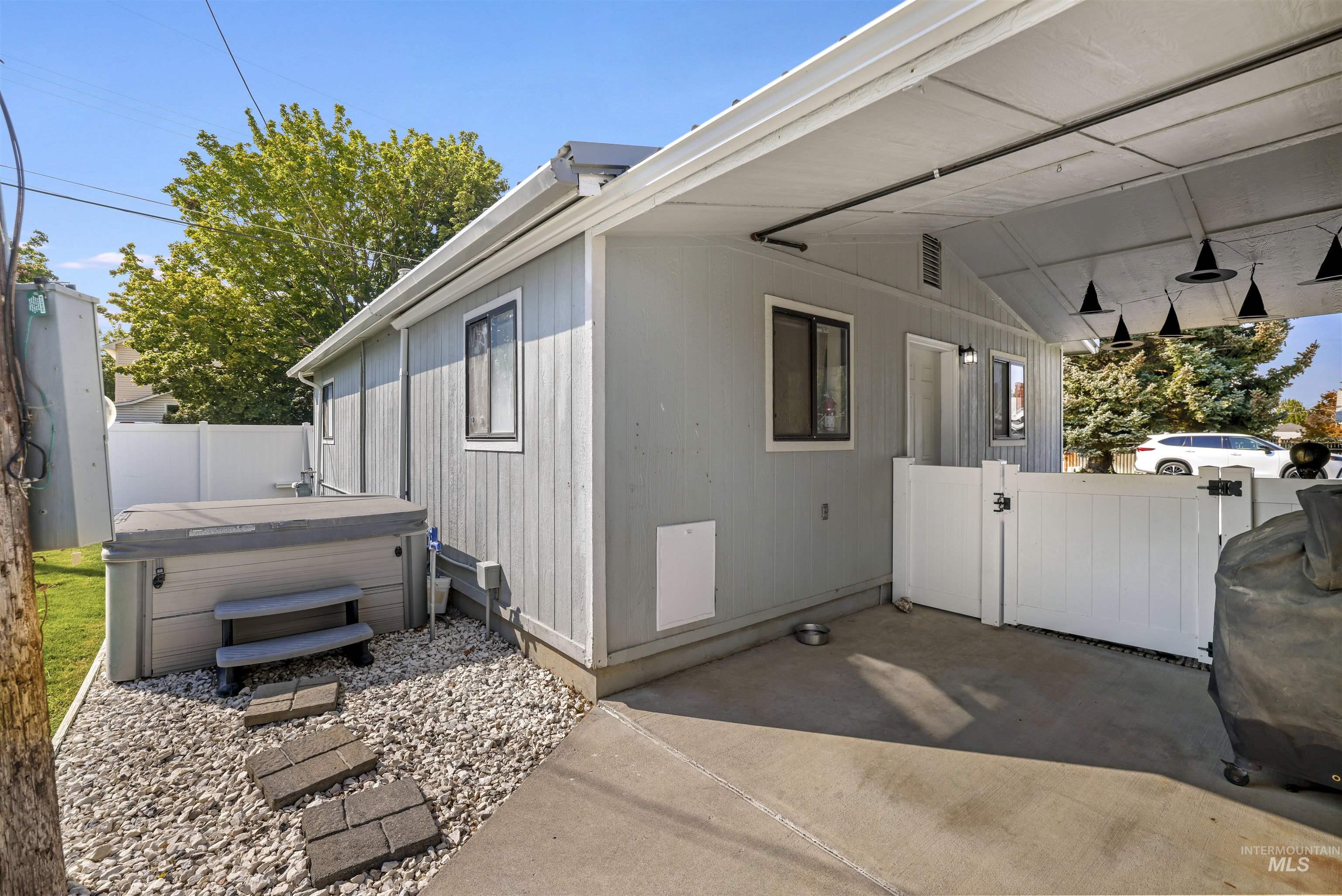 View of property exterior featuring a gate, a hot tub, and a patio