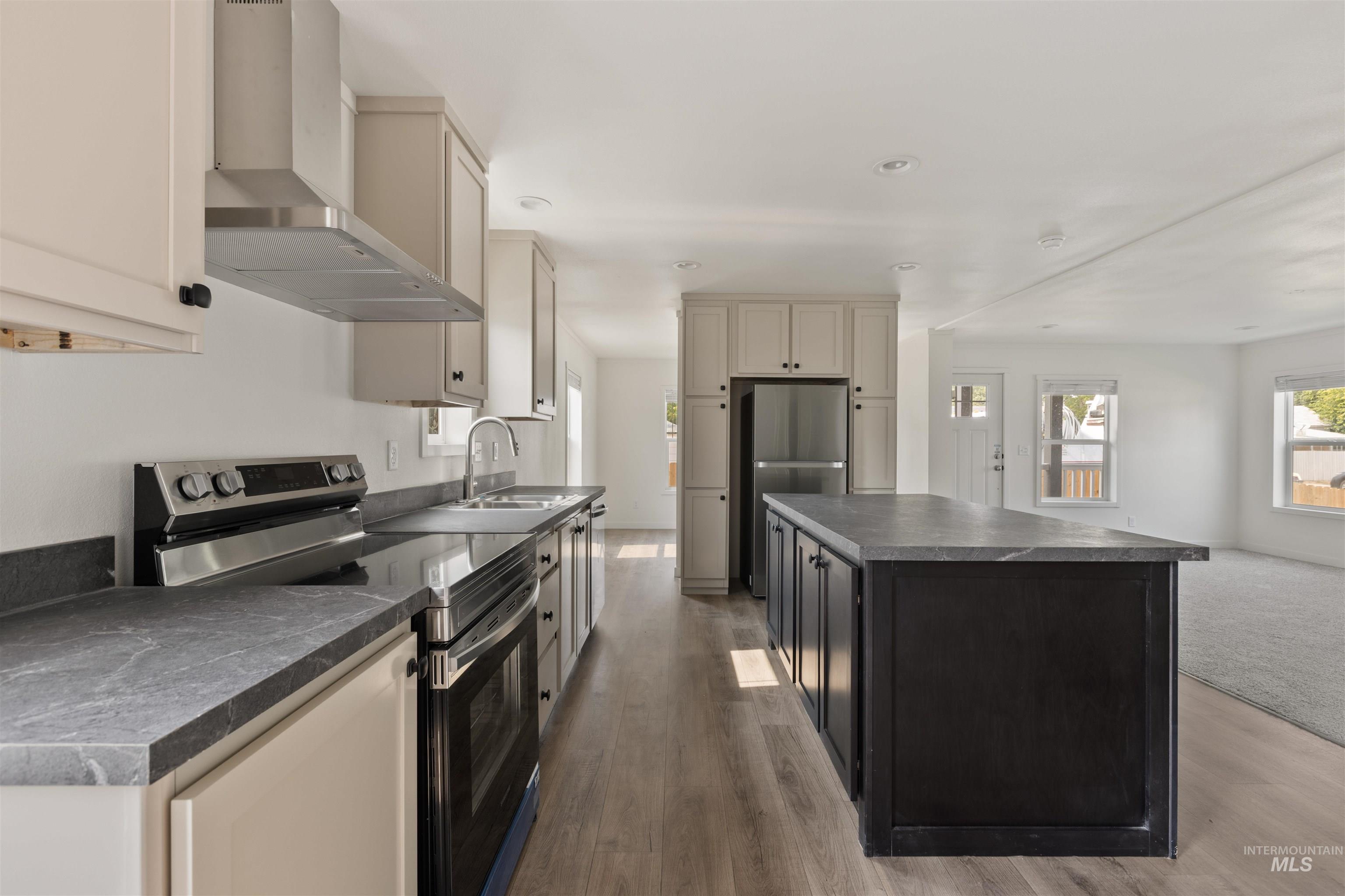 Kitchen featuring dark countertops, appliances with stainless steel finishes, wall chimney range hood, a center island, and dark cabinetry