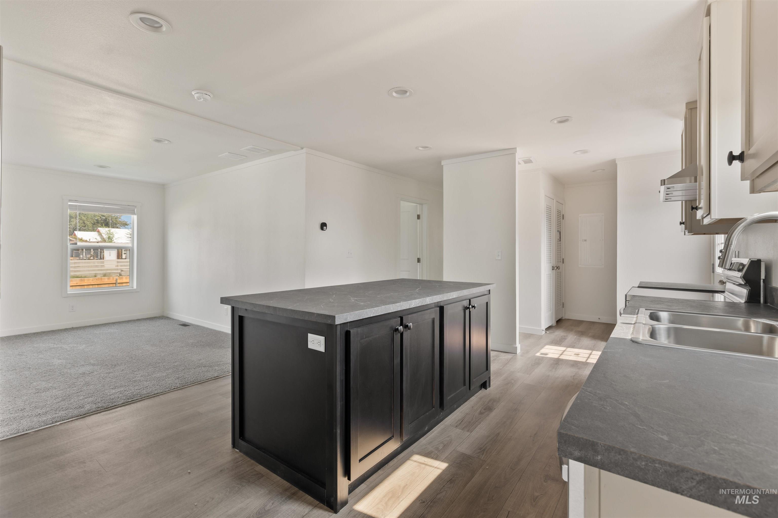 Kitchen with dark countertops, dark cabinets, open floor plan, light wood finished floors, and recessed lighting