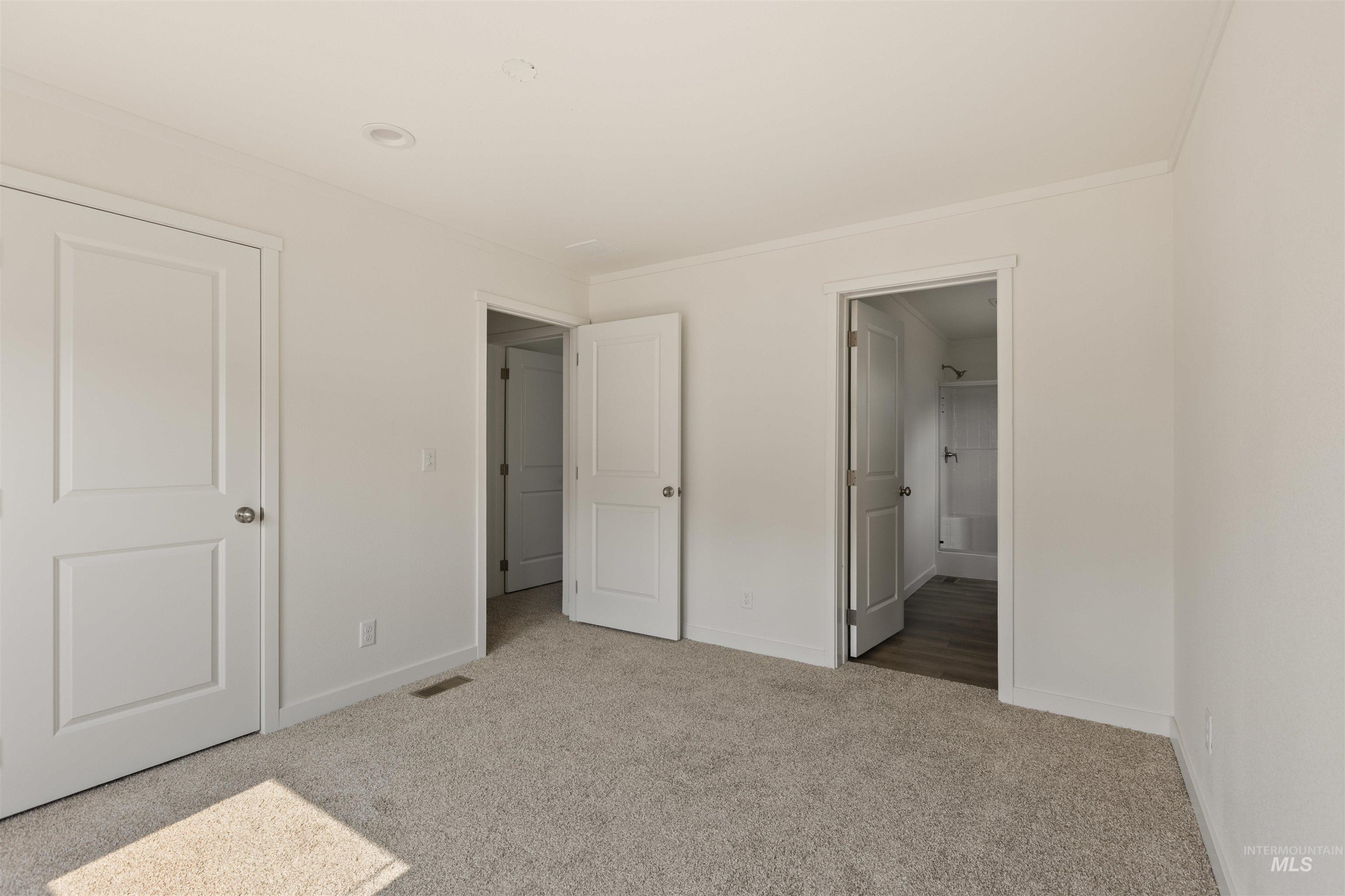Unfurnished bedroom with ensuite bathroom and light carpet