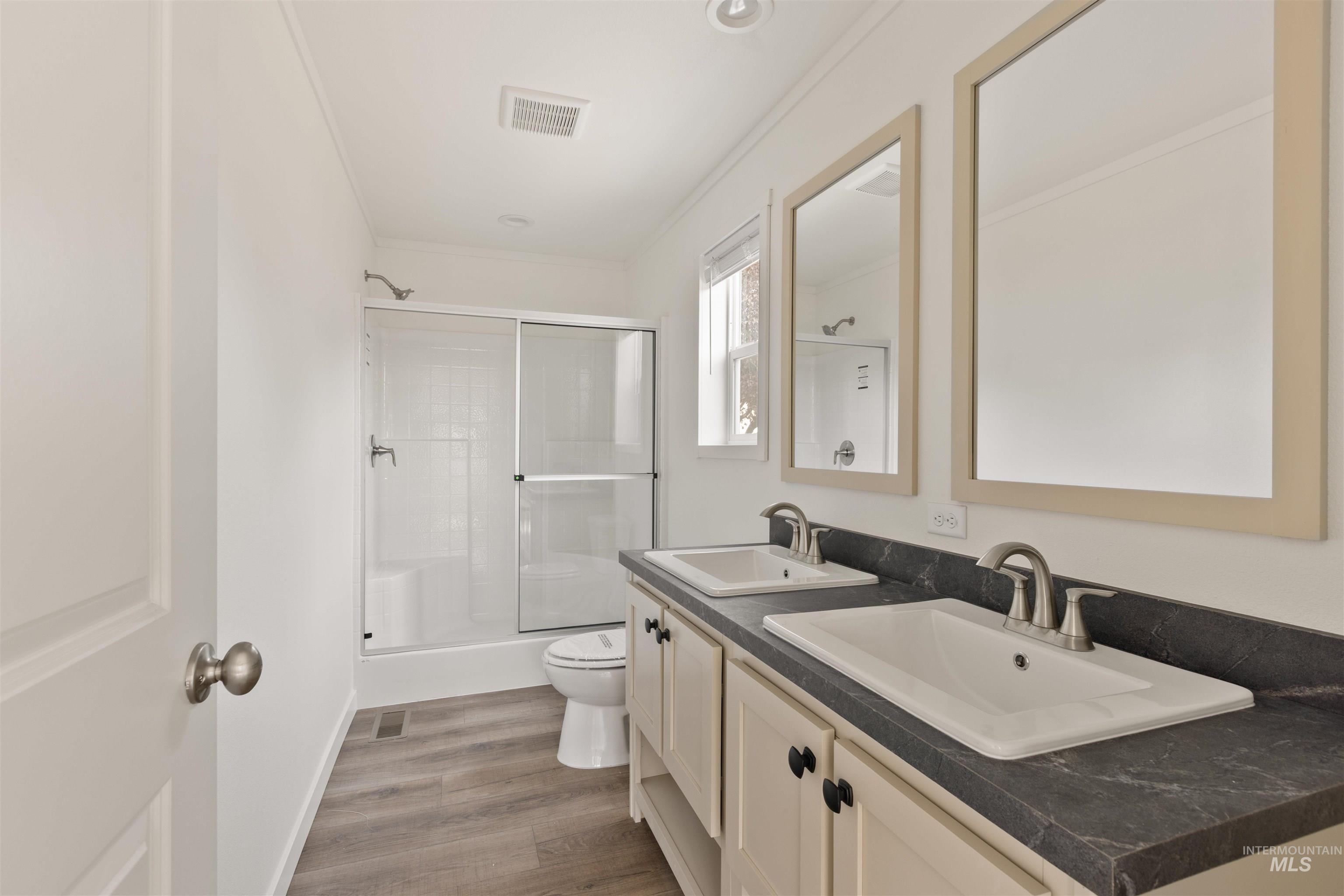Bathroom with dark wood-type flooring, double vanity, shower / bath combination with glass door, ornamental molding, and recessed lighting