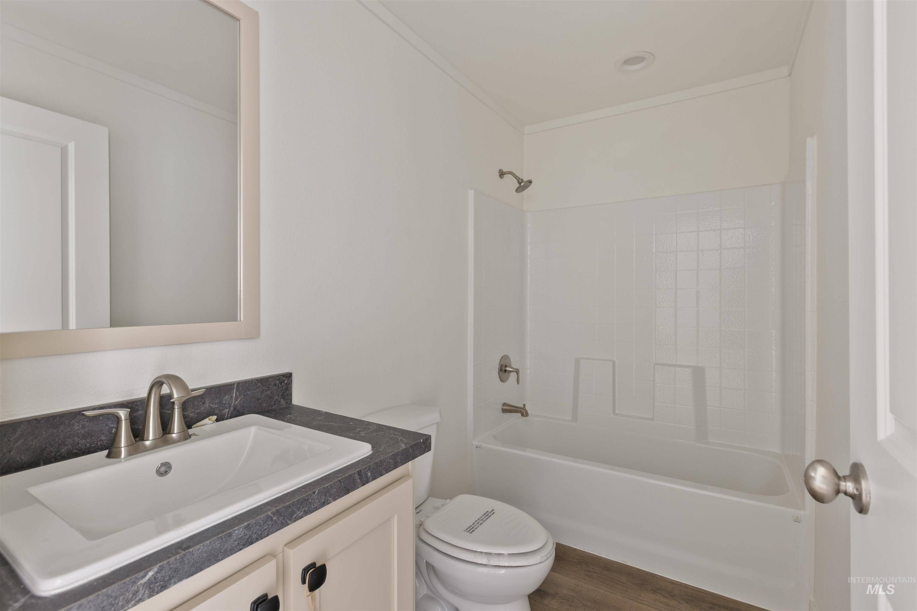 Full bath with vanity,  shower combination, dark wood-style flooring, and ornamental molding