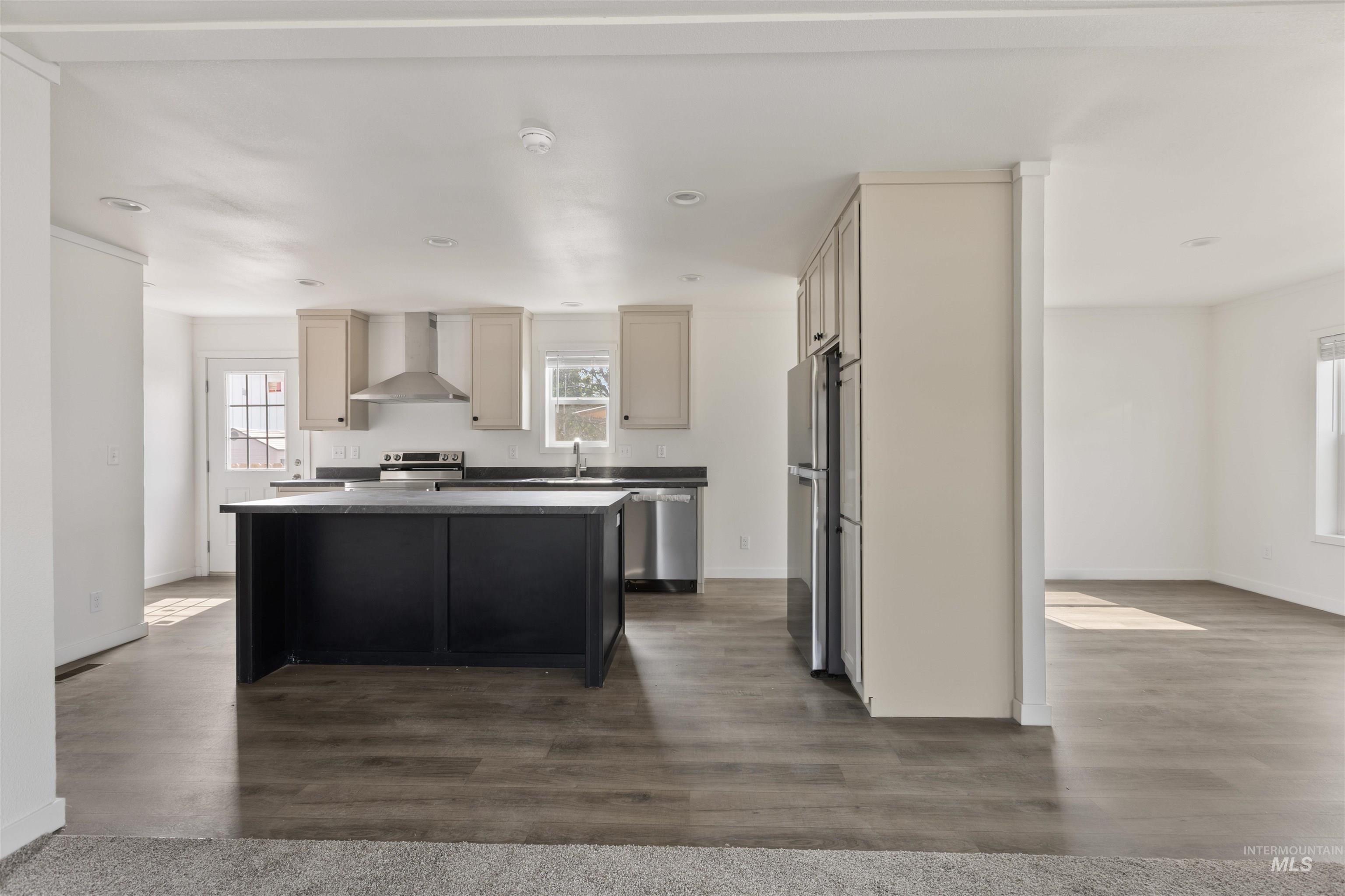 Kitchen featuring cream cabinets, dark cabinets, wall chimney range hood, dark wood-style floors, and recessed lighting