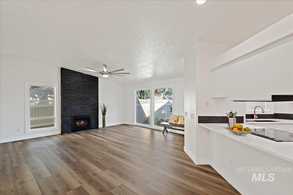Living room with light wood-style floors, a large fireplace, a textured ceiling, ceiling fan, and lofted ceiling