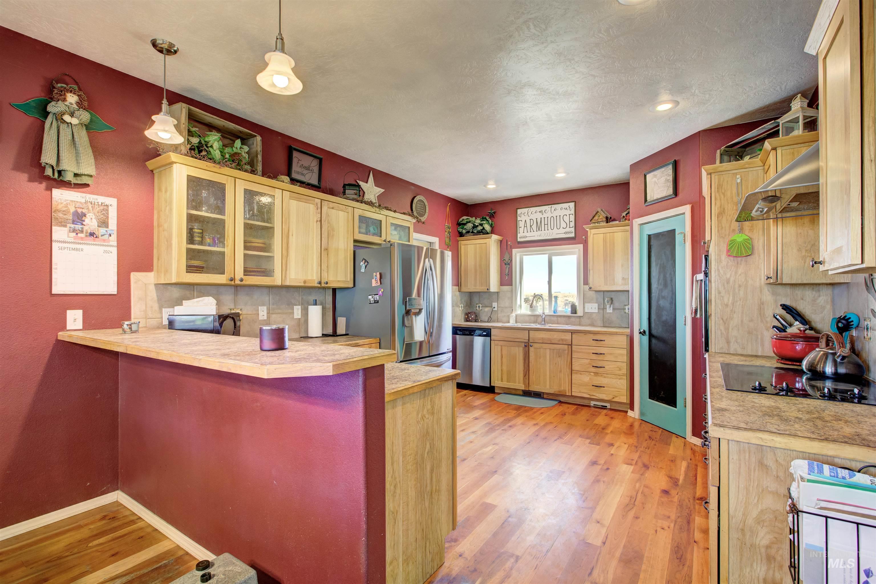 Kitchen with light countertops, glass insert cabinets, a peninsula, light wood finished floors, and stainless steel appliances