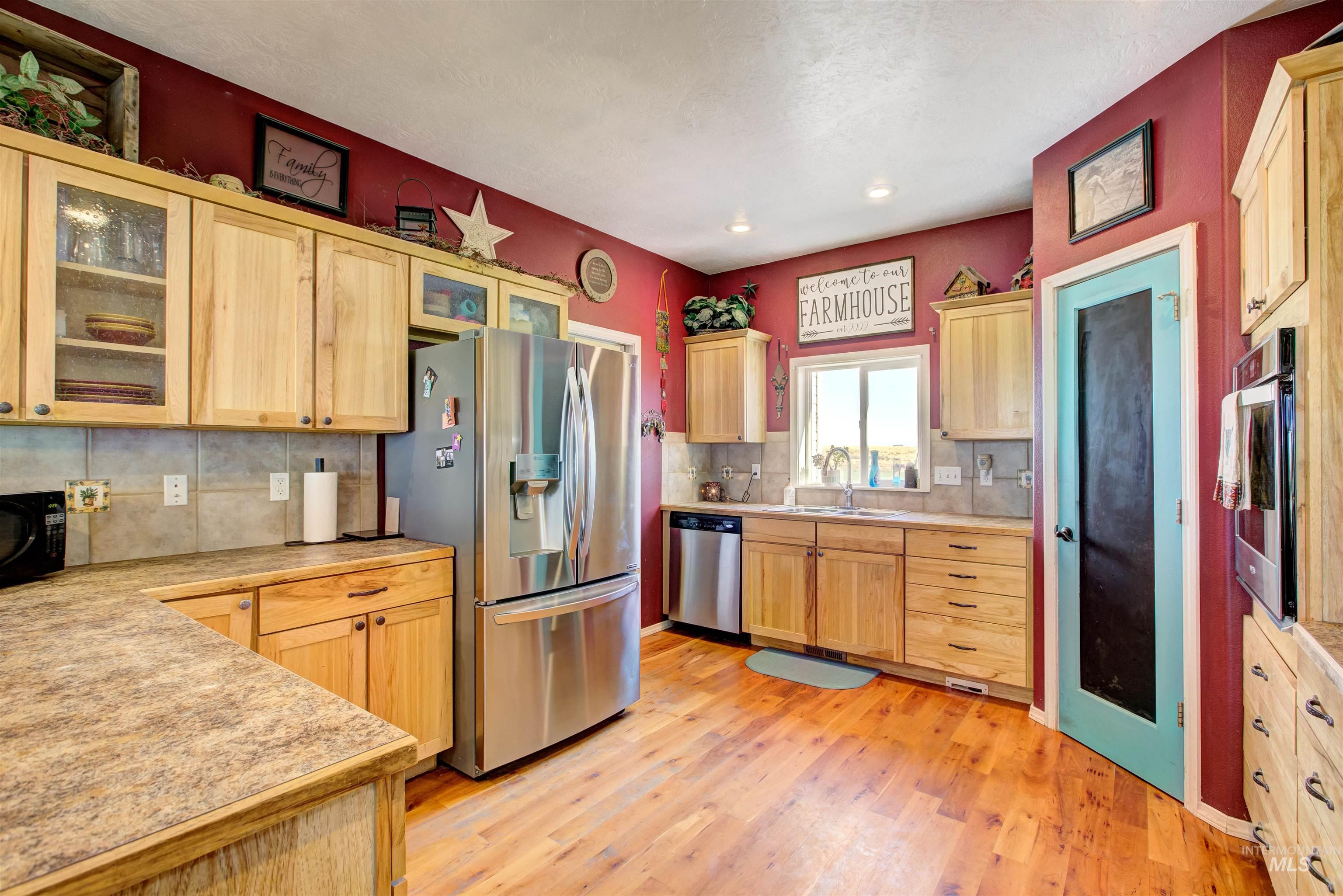 Kitchen featuring light brown cabinetry, glass insert cabinets, stainless steel appliances, tasteful backsplash, and recessed lighting