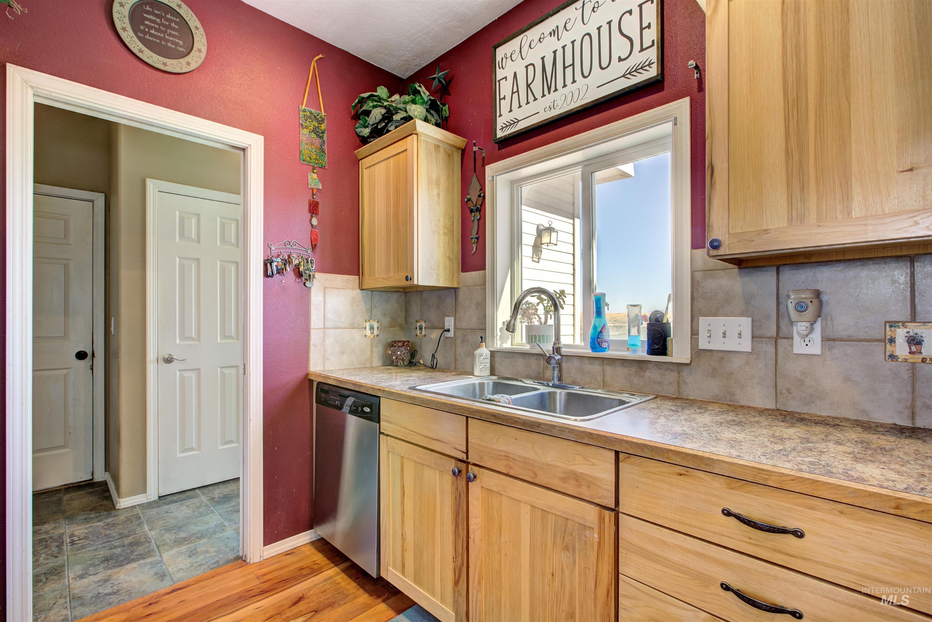 Kitchen with light countertops, decorative backsplash, light brown cabinetry, and stainless steel dishwasher